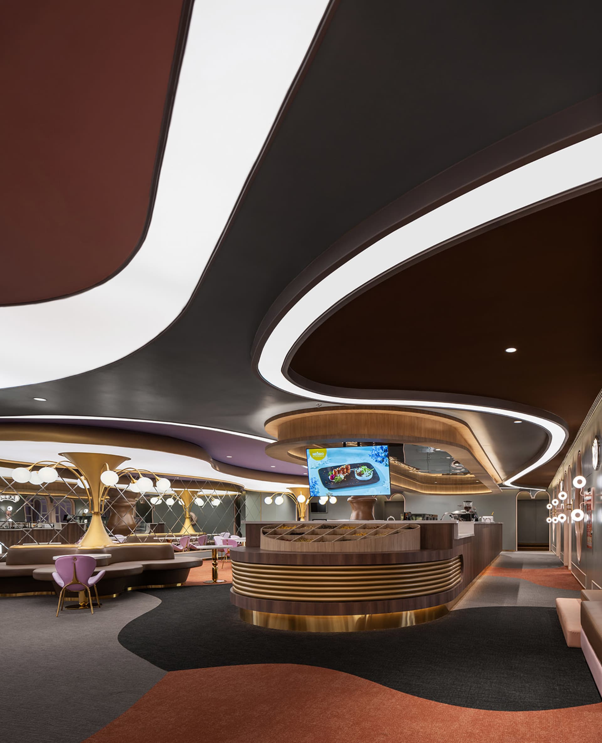 A modern restaurant bar with brass and glass accents, featuring a circular bar counter and large, curved ceiling lights.