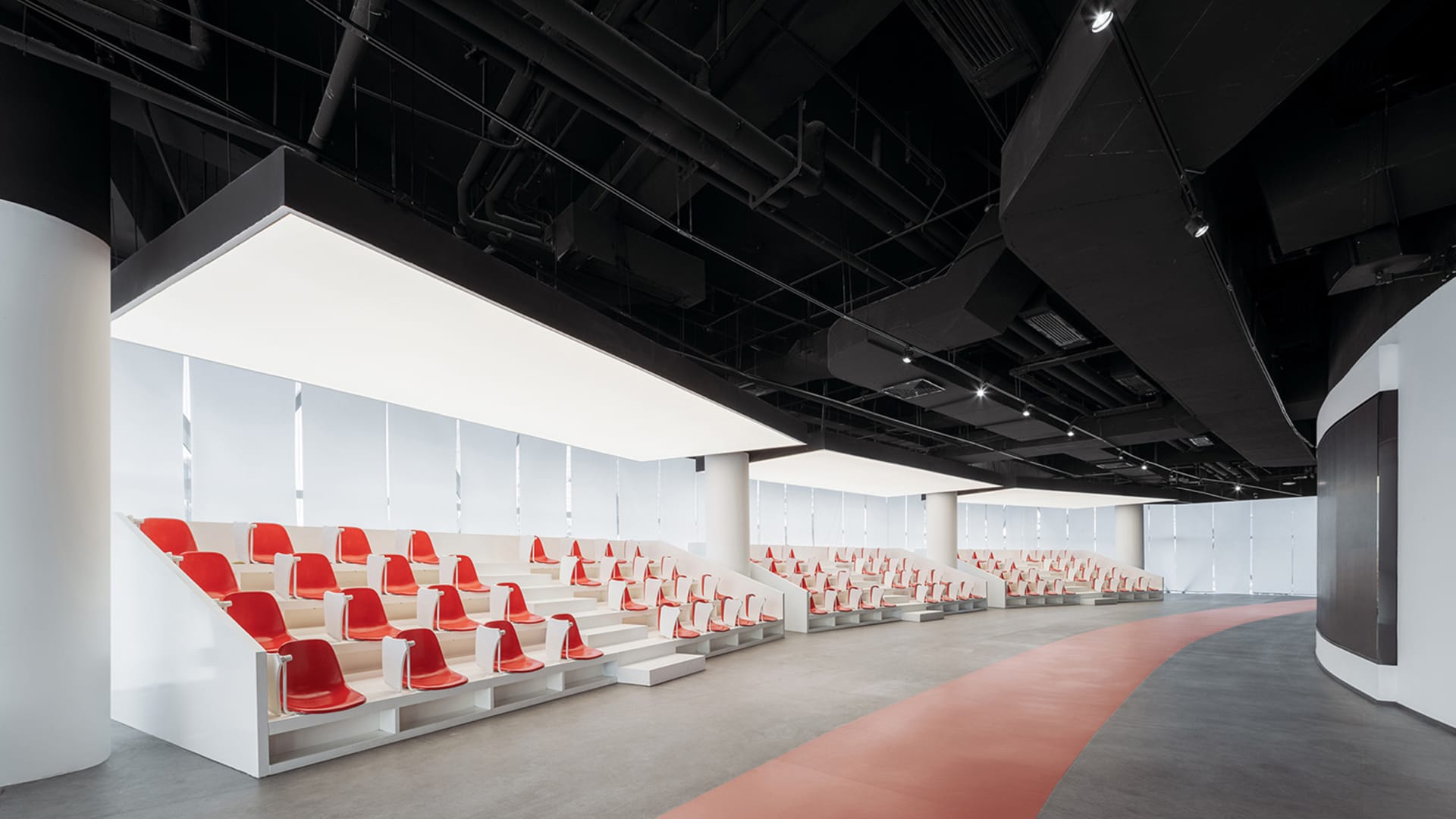 A modern event hall with concrete architecture, white seating, and red accents.