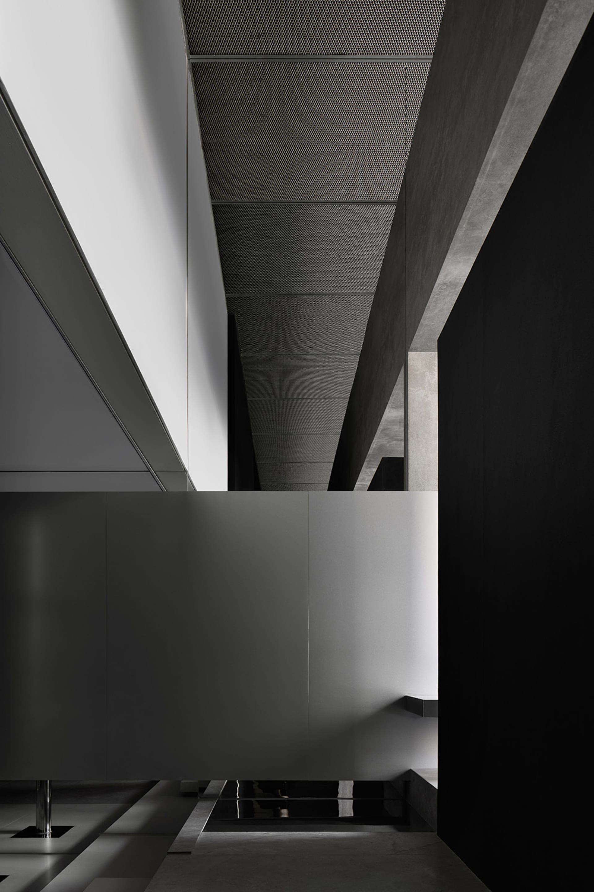 A minimalist, modern interior corridor with concrete walls and flooring, featuring a sleek, open design and a geometric ceili