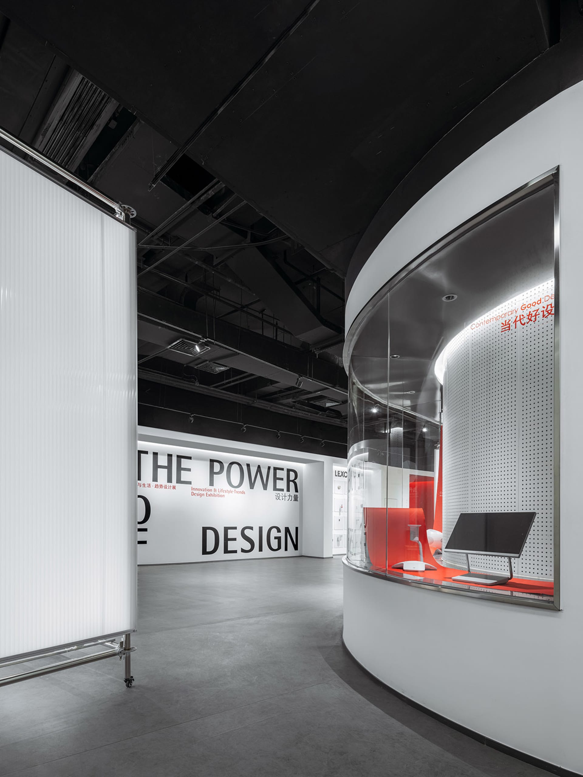 A minimalist exhibition space with white walls and a curved glass wall.