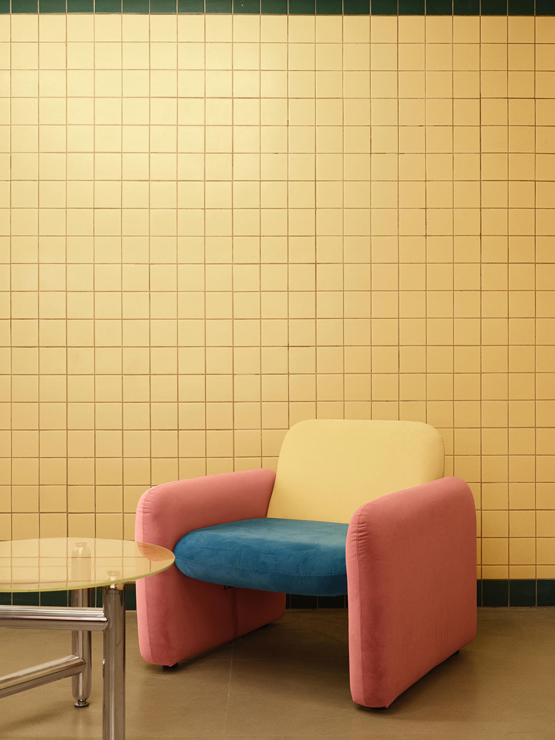 A modern living room with a pink and blue armchair against a yellow tiled wall.
