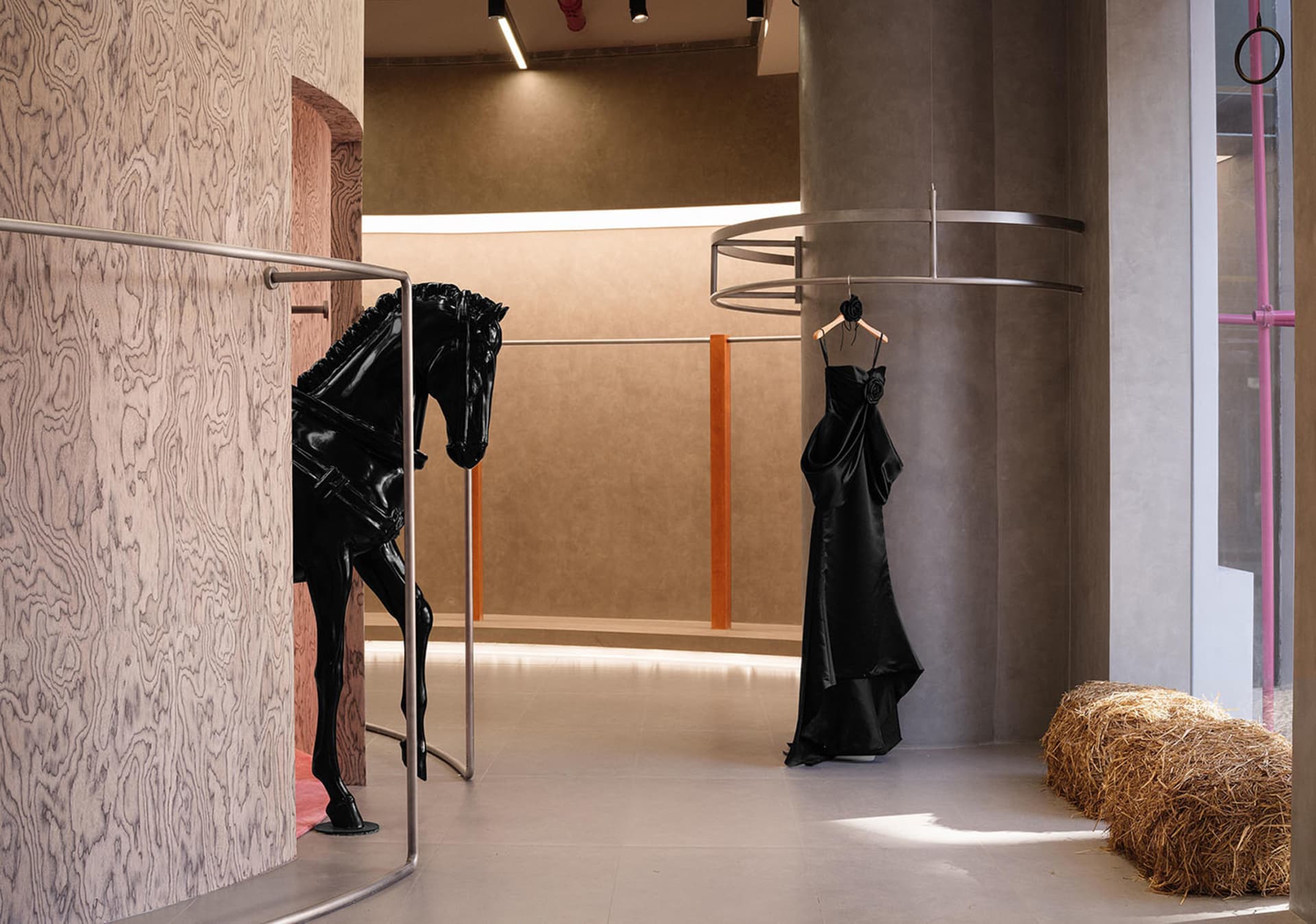 An elegant fashion boutique interior featuring a black horse statue, a black dress hanging on a circular rack, and a bale of