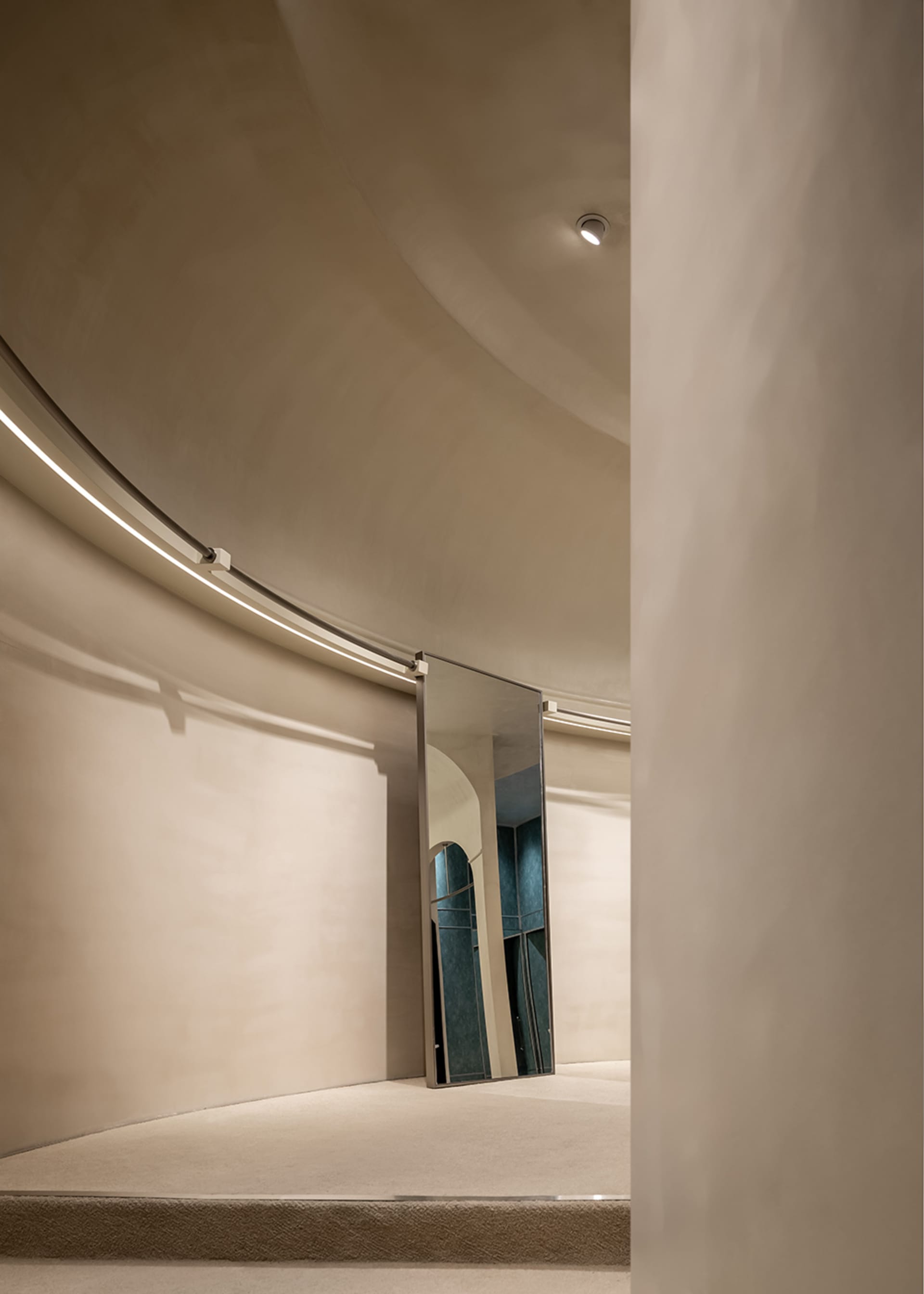 A modern interior space with curved walls and neutral materials, including a reflective mirror.