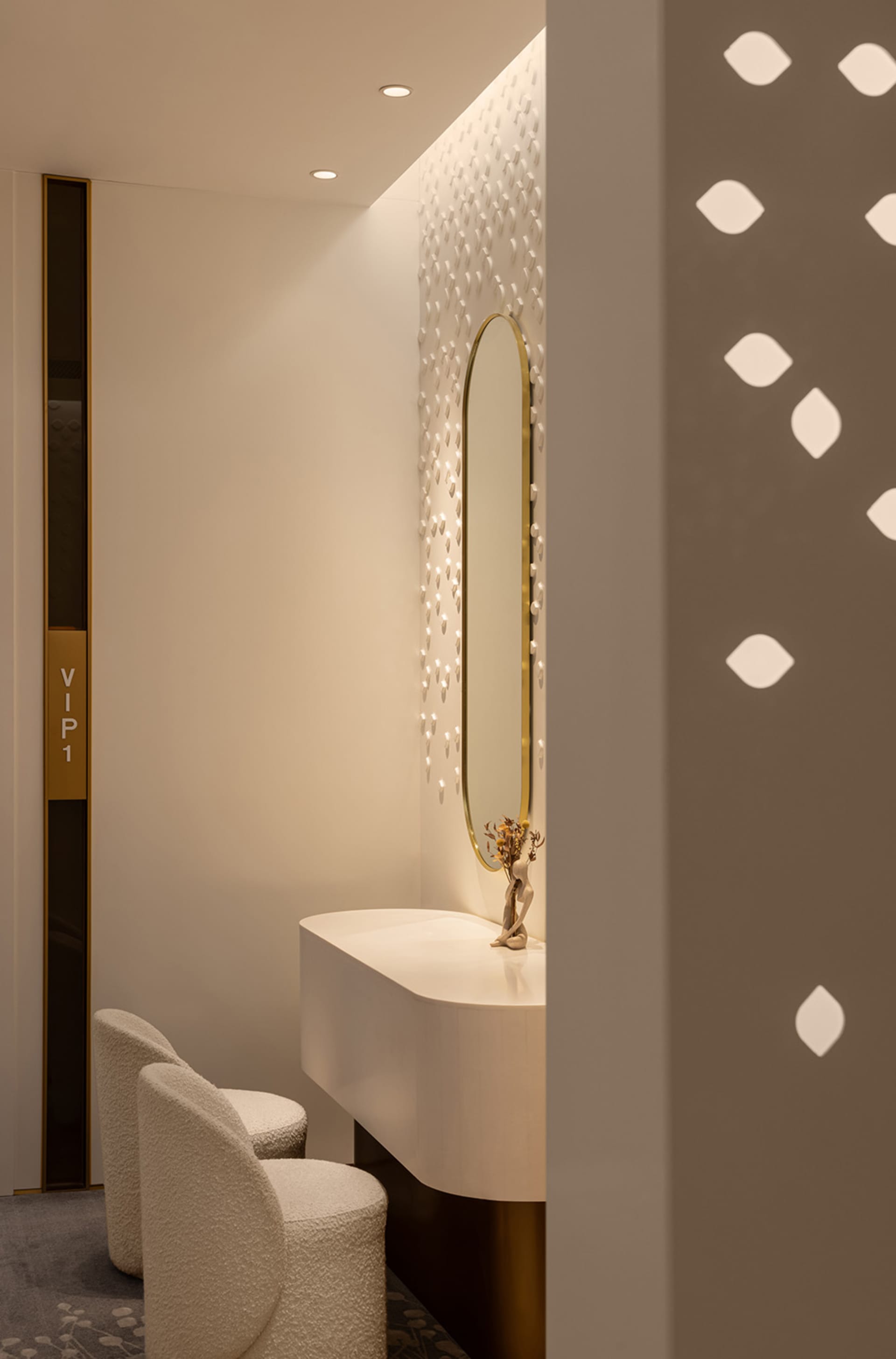 A modern hotel suite with white furniture, a vanity area with an oval mirror and decorative lighting, and a textured carpet.
