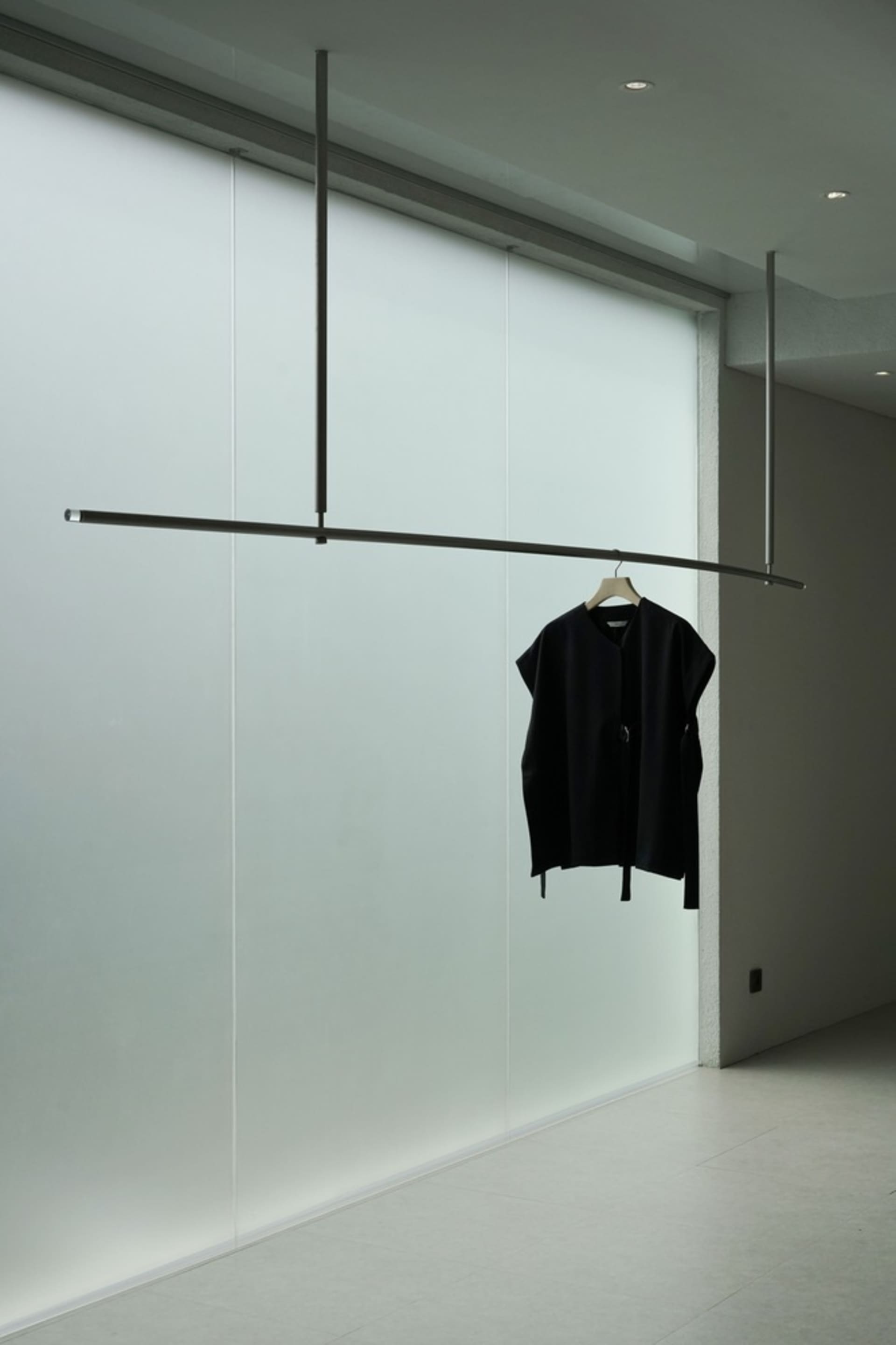 極簡服裝展示,單件黑色服裝懸掛於懸吊式衣桿上。