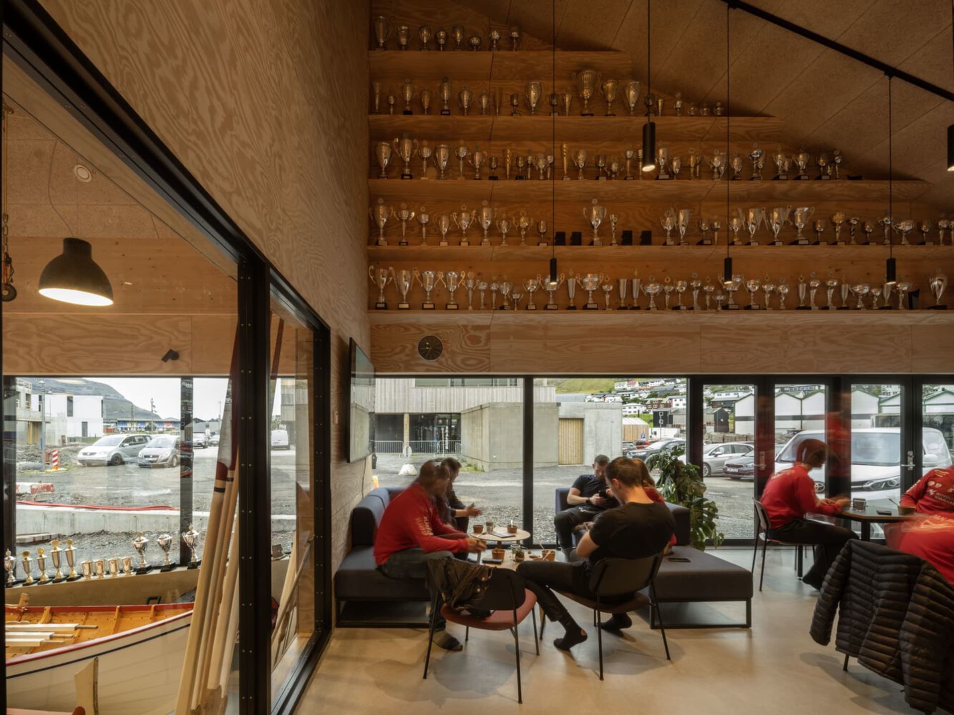 People sitting in an industrial-style cafe with wooden walls, glass trophies, and metal furniture.