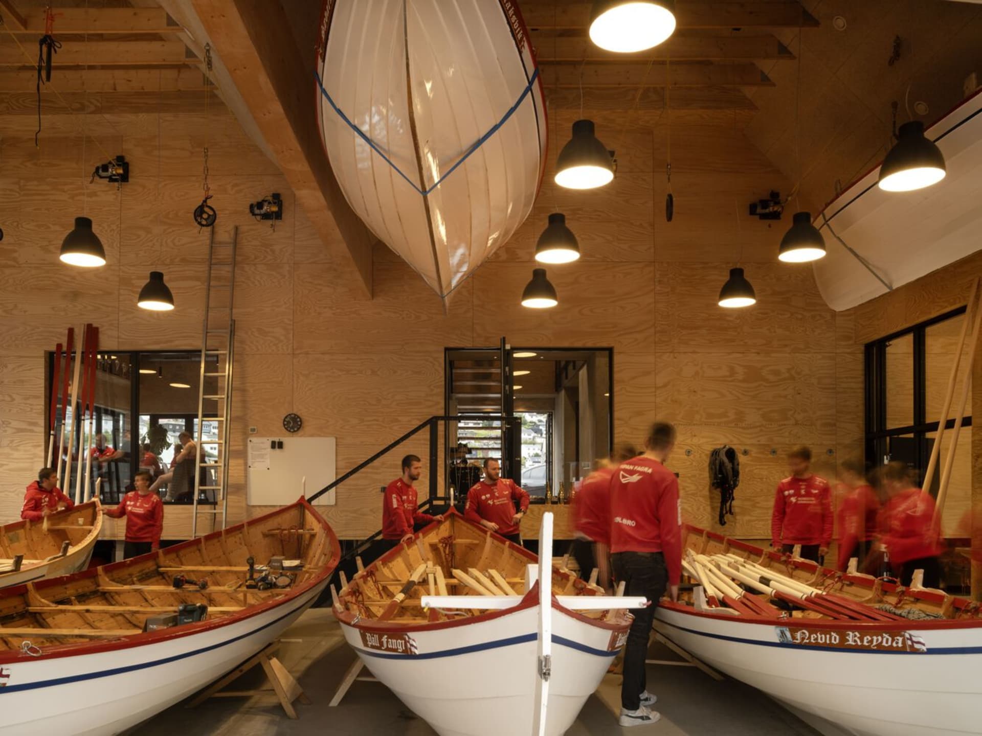 People working in a modern boating center with boats, oars, and wooden structures.