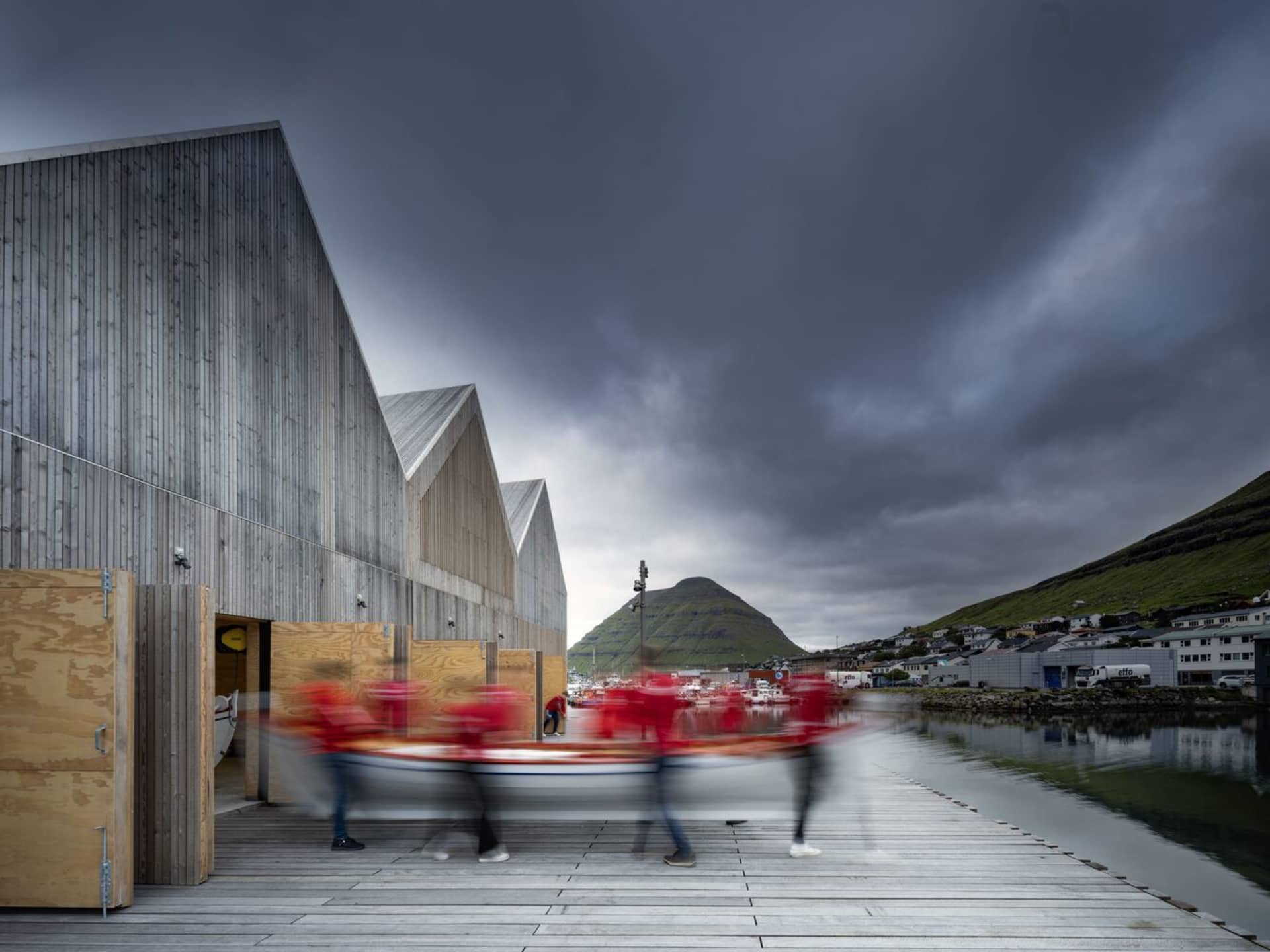 People pulling a small boat on wooden dock, modern architectural buildings in the background.