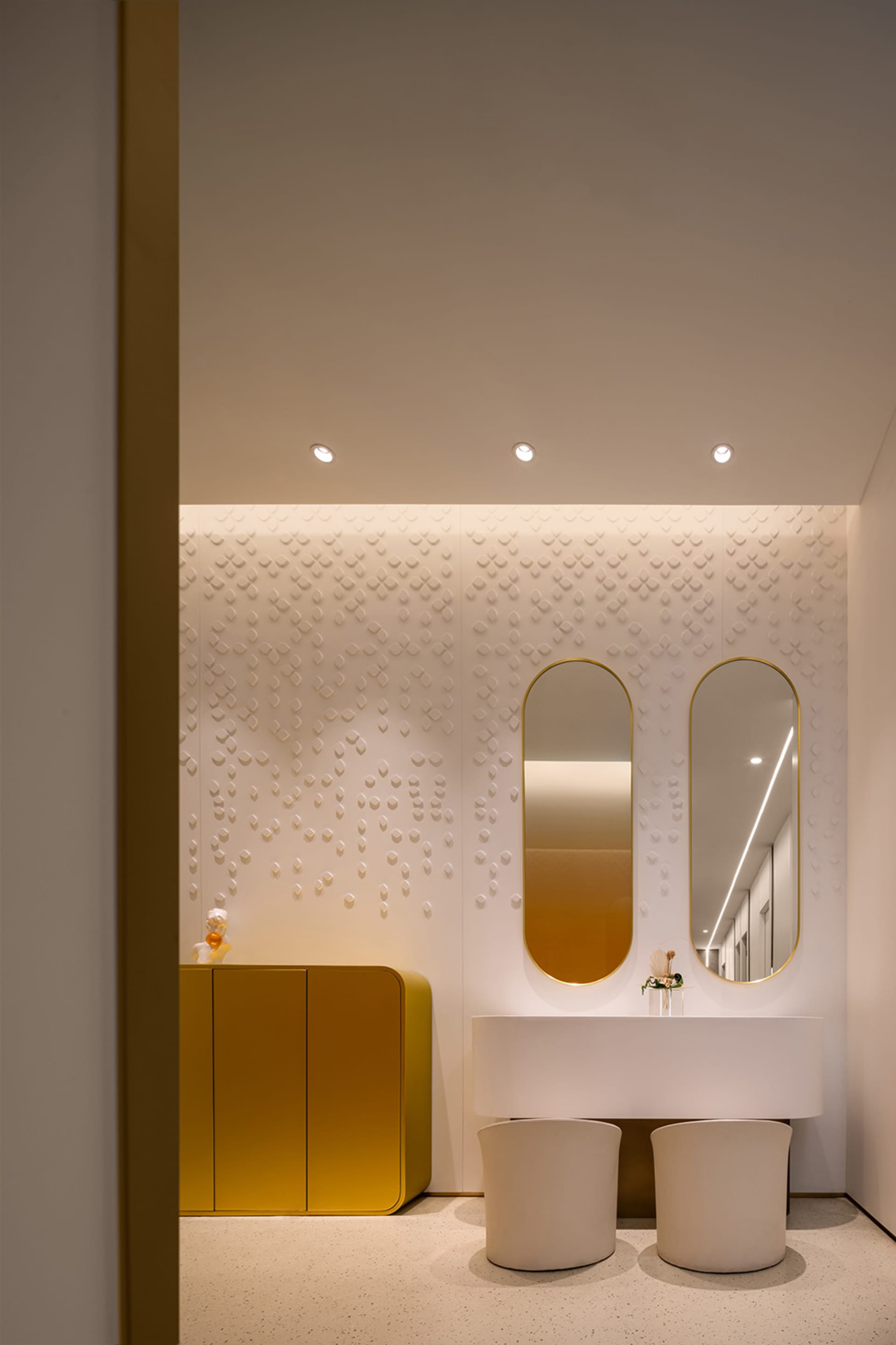 Modern bathroom design featuring a white concrete vanity with two curved mirrors above it, a gold cabinet, and a textured whi