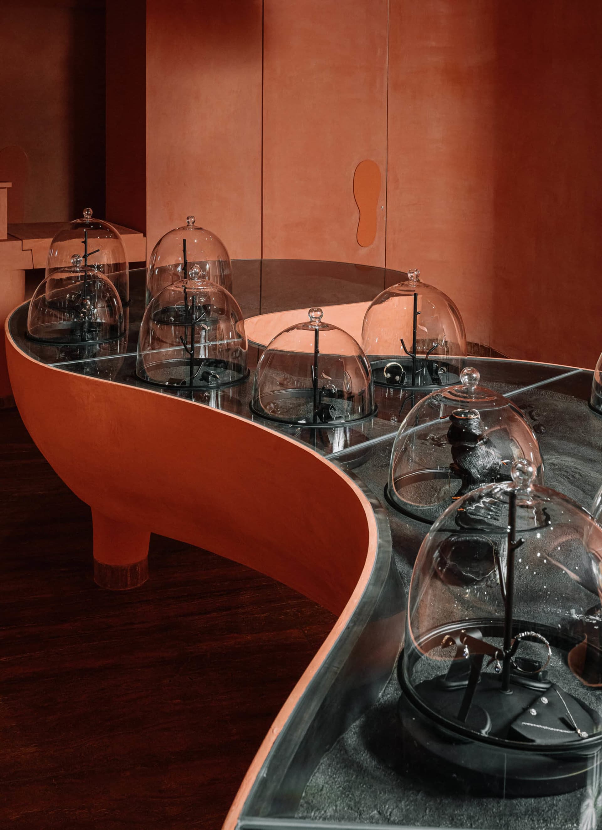 Multiple glass domes showcasing jewelry on a curved, red wooden platform.