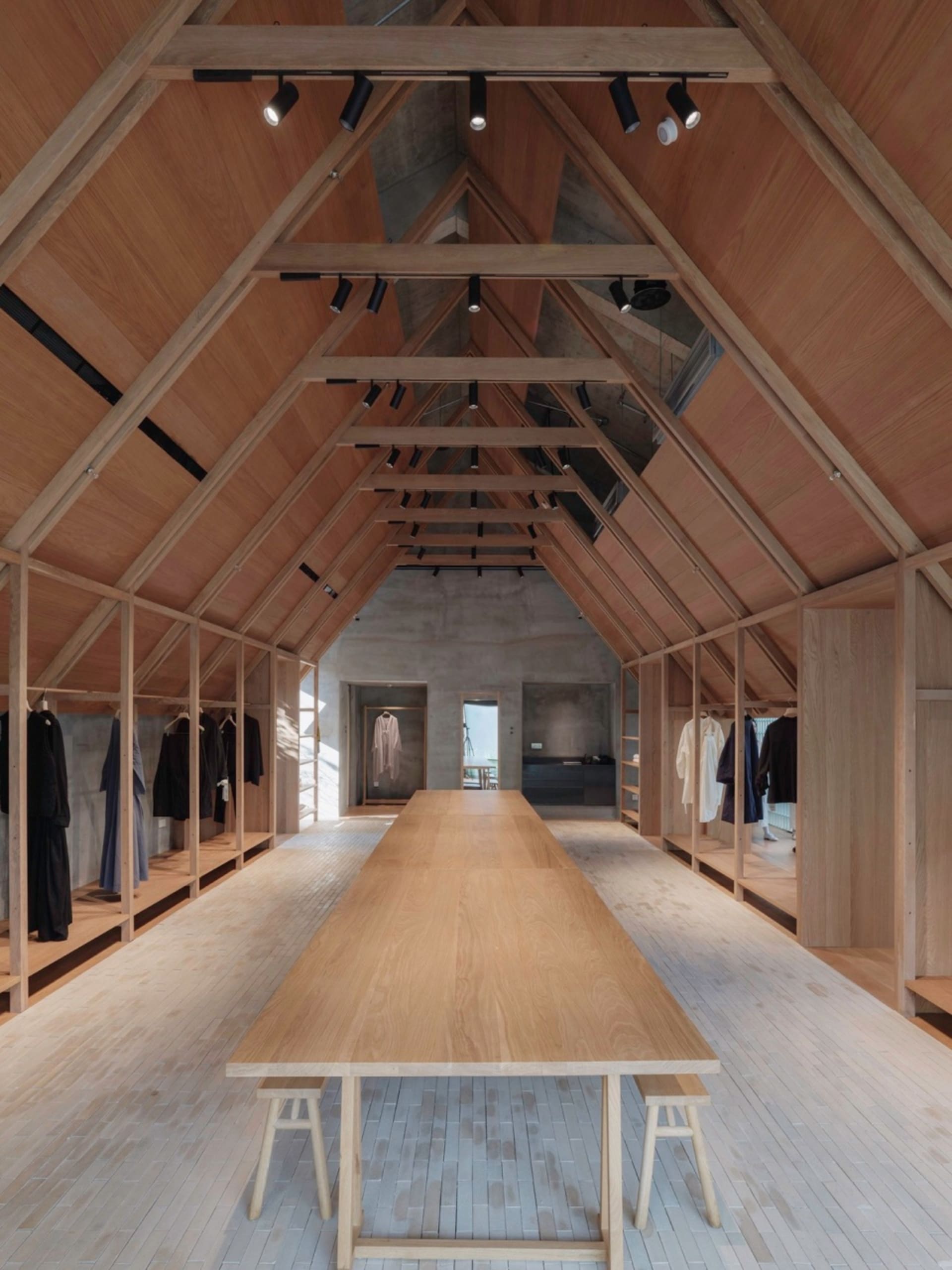 A minimalist clothing shop with wooden elements and a sloped, wooden ceiling structure.