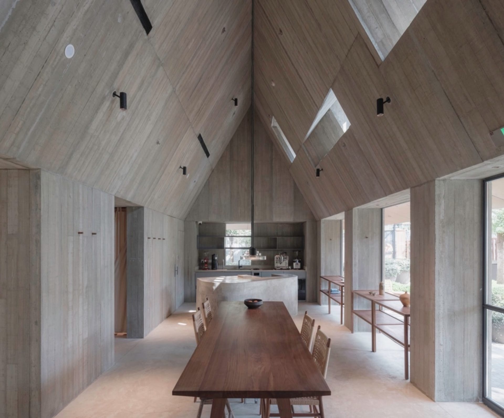 極簡住宅廚房,裸露混凝土牆面與天花板,搭配大型木製餐桌與餐椅。