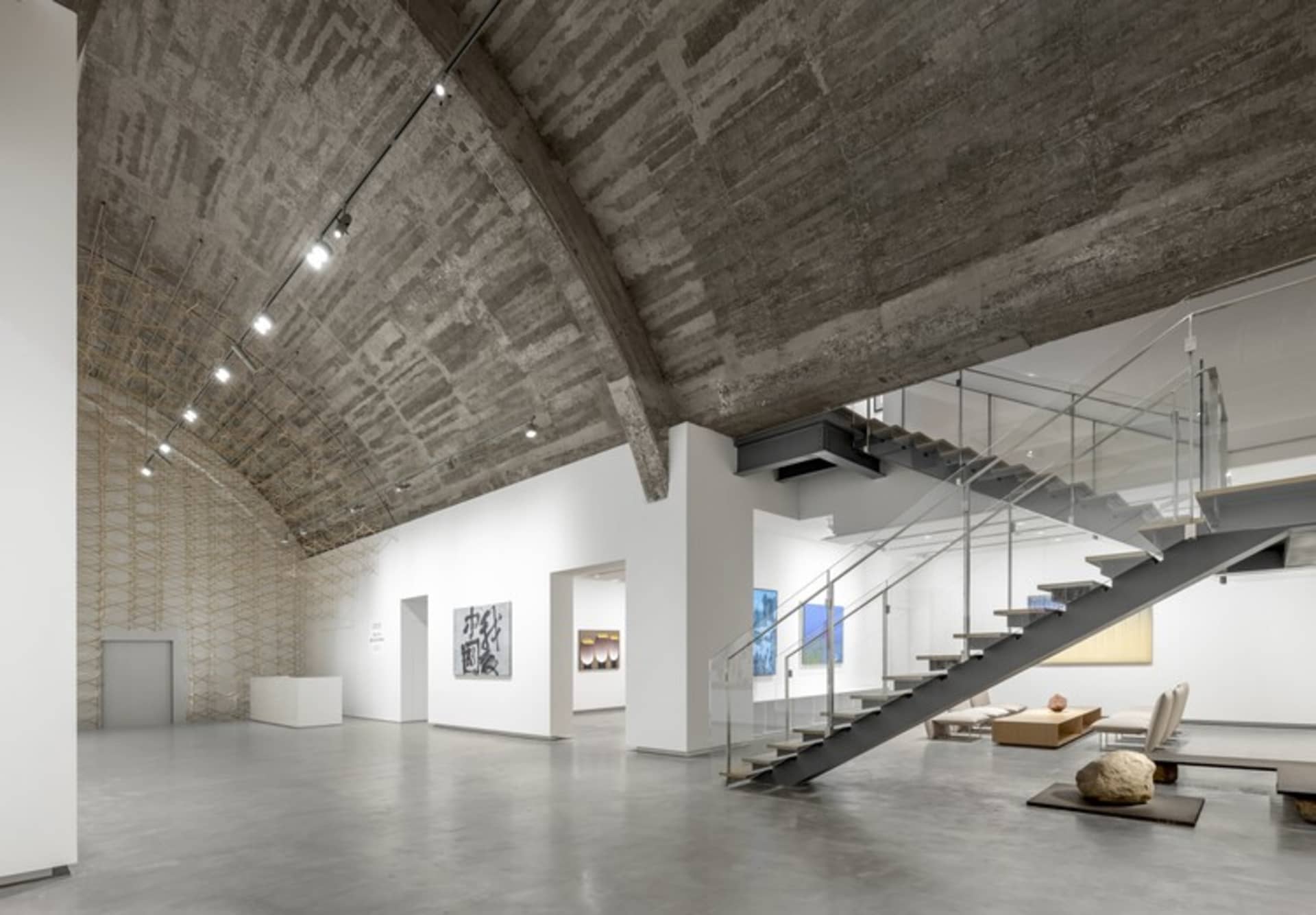 Modern museum exhibition space featuring a concrete ceiling and stairs.