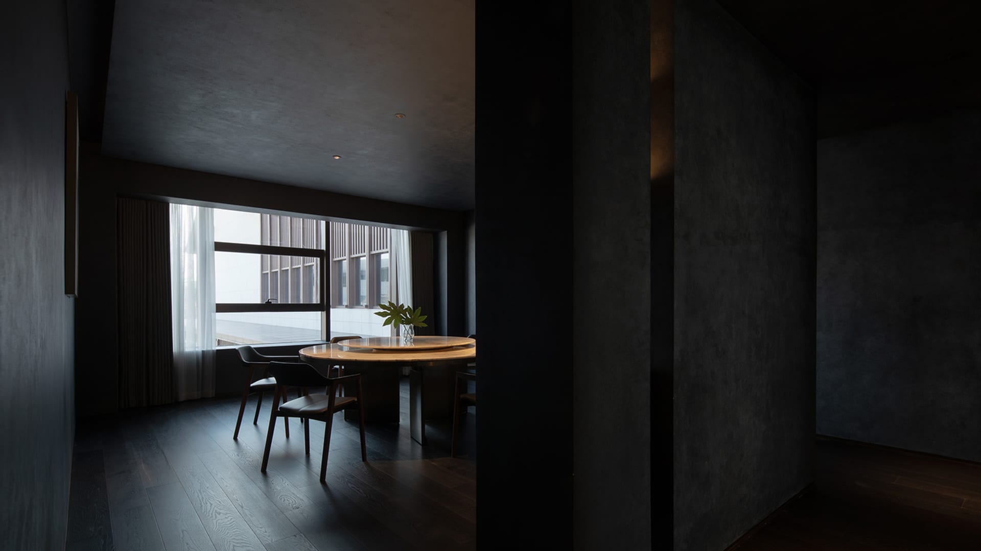 Interior photograph of a modern dark dining room with dark wood flooring and a round table.