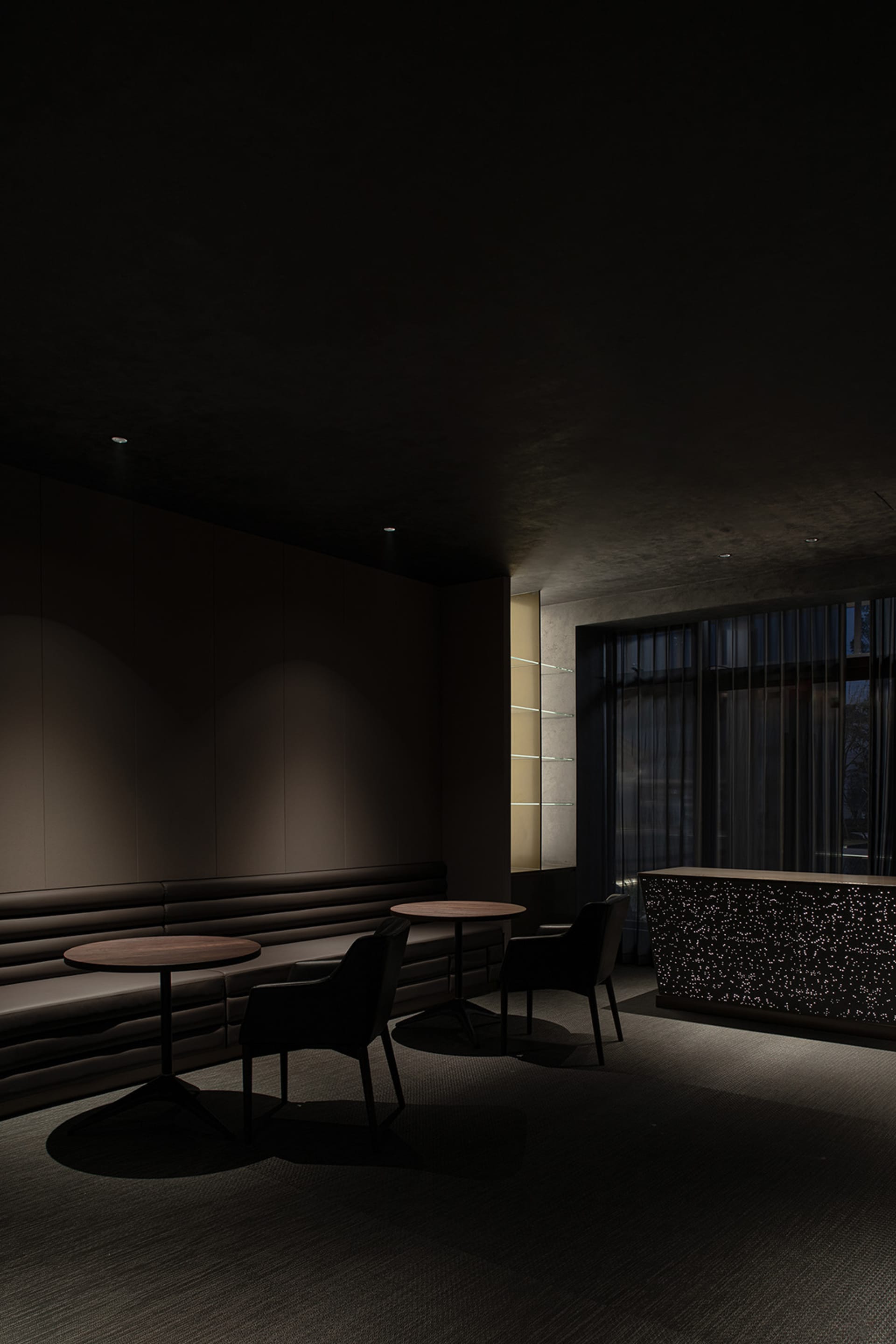 A sleek, dark-themed hotel lounge with modern furniture and dark stone finishes.