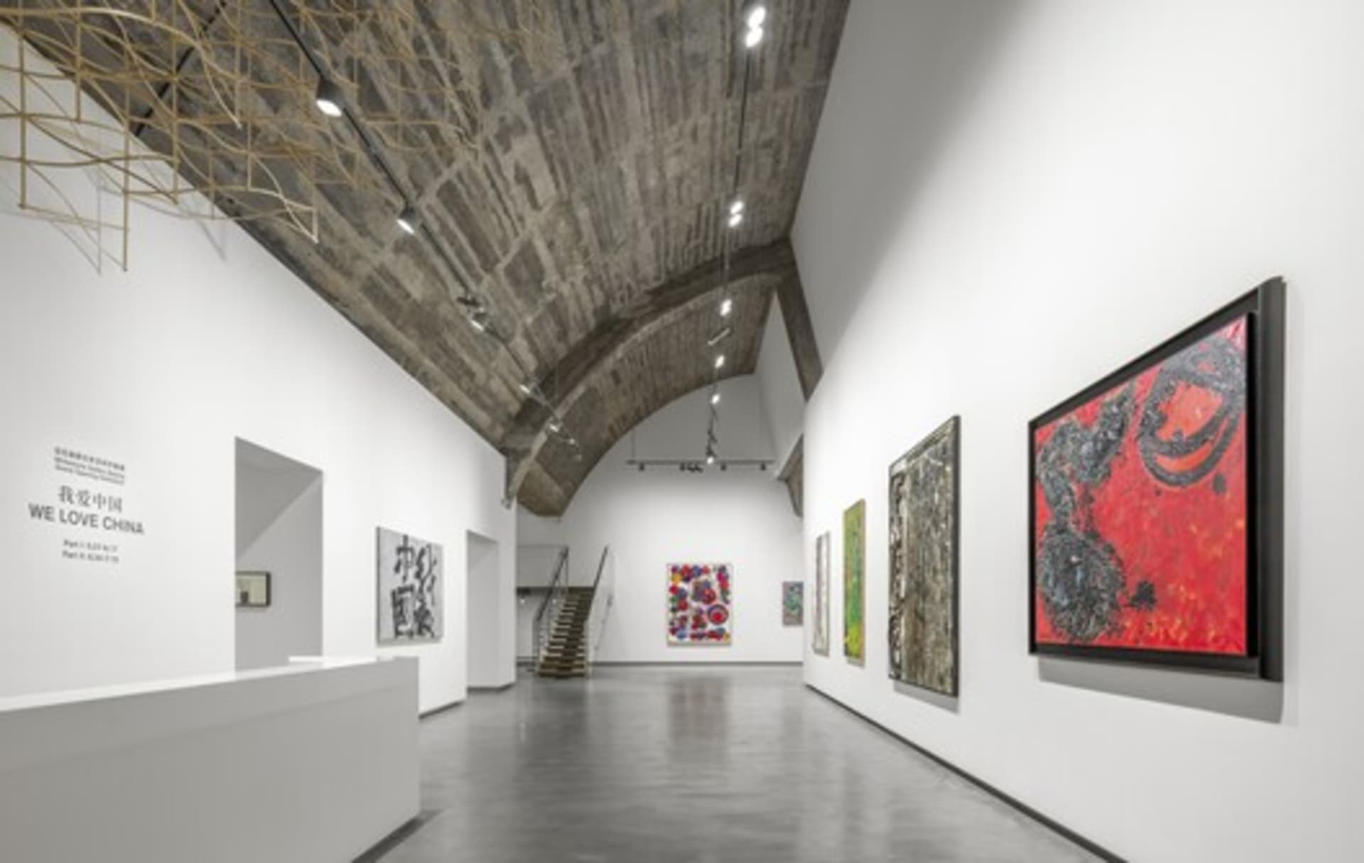 現代工業風藝術畫廊,混凝土牆面搭配鋼梁,牆上展示多件藝術作品。