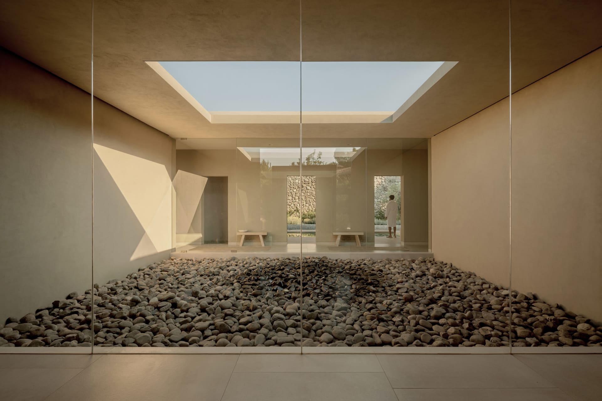 A minimalist room with concrete walls, glass walls, and a stone floor, featuring a skylight.