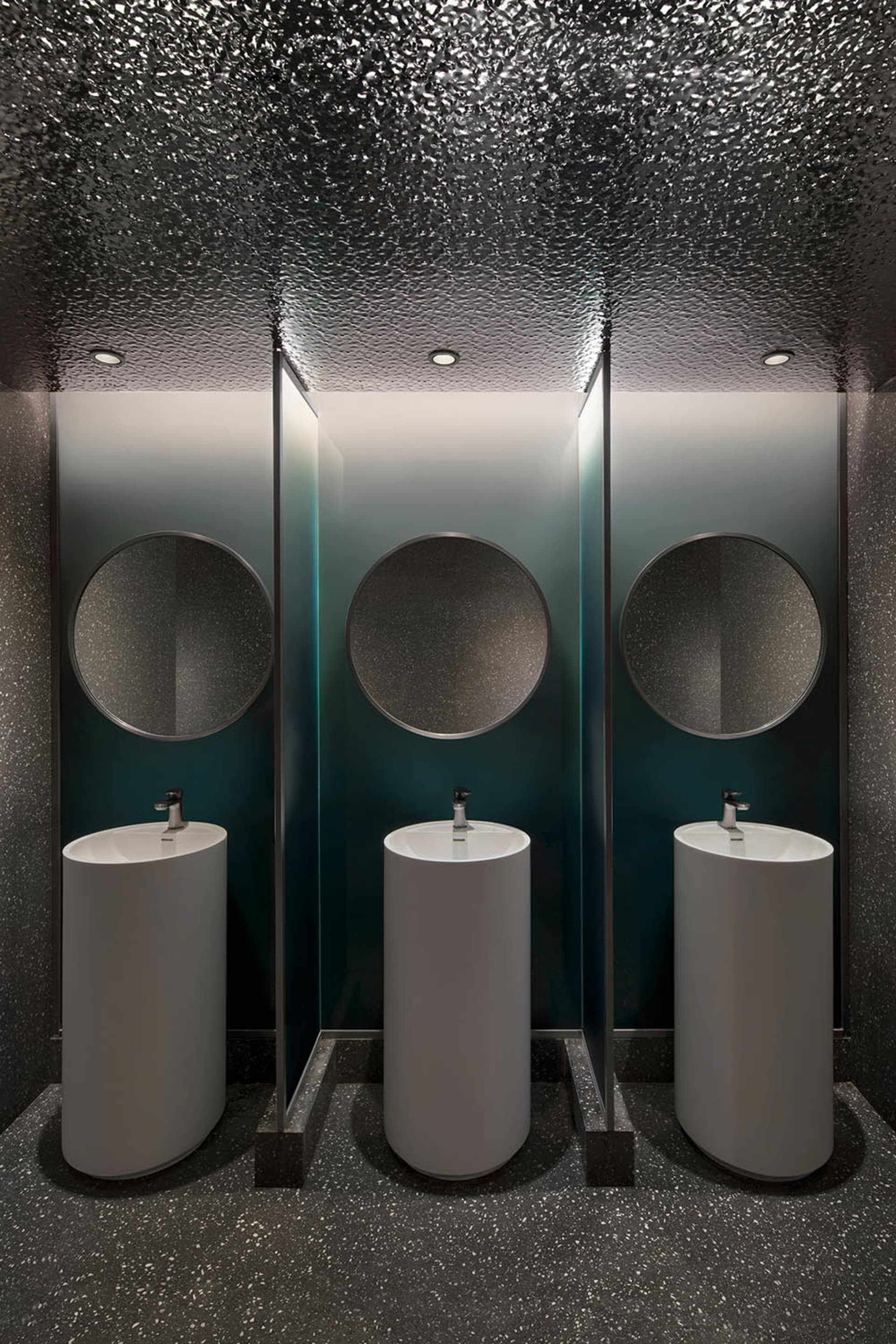 Modern bathroom interior with white circular sinks, terrazzo flooring, and round mirrors.