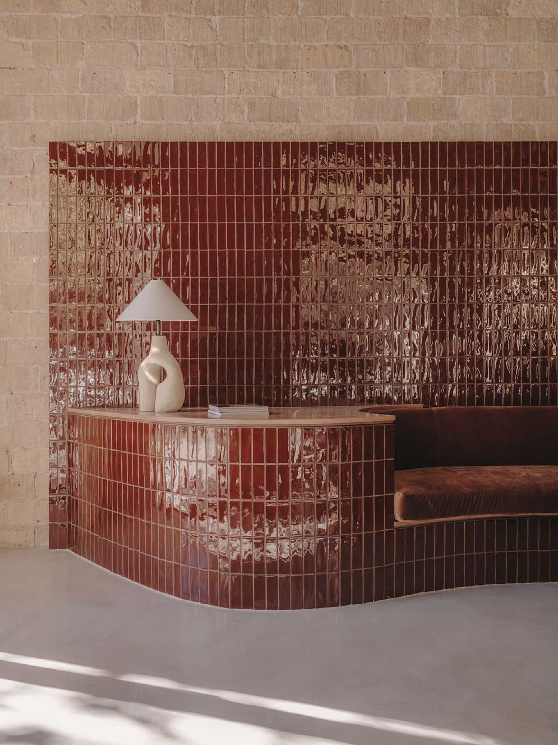 A modern living room featuring ceramic tiles, a curved seating area, and a unique table lamp.