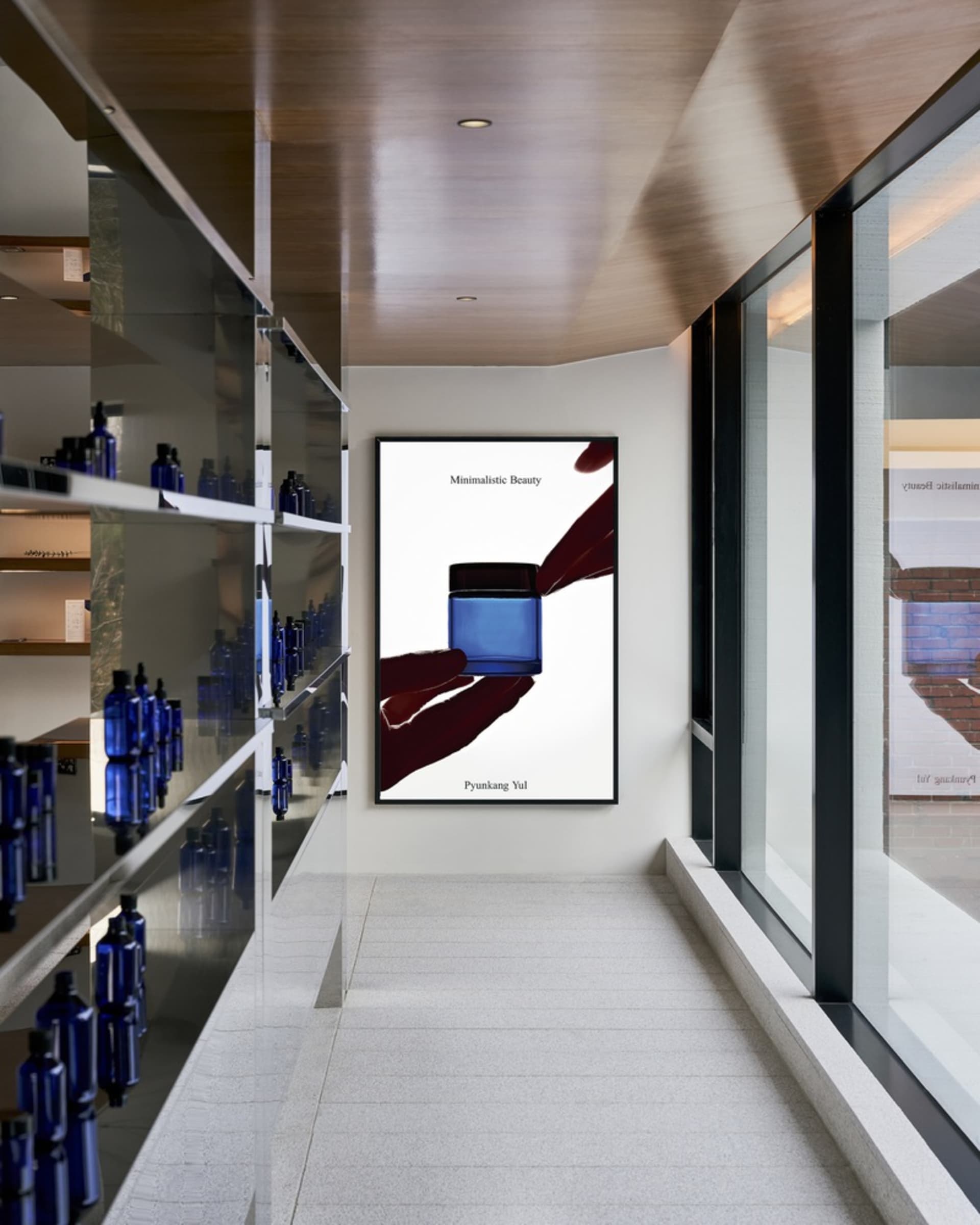 A modern minimalist interior featuring glass shelves displaying various bottles of cosmetic products.