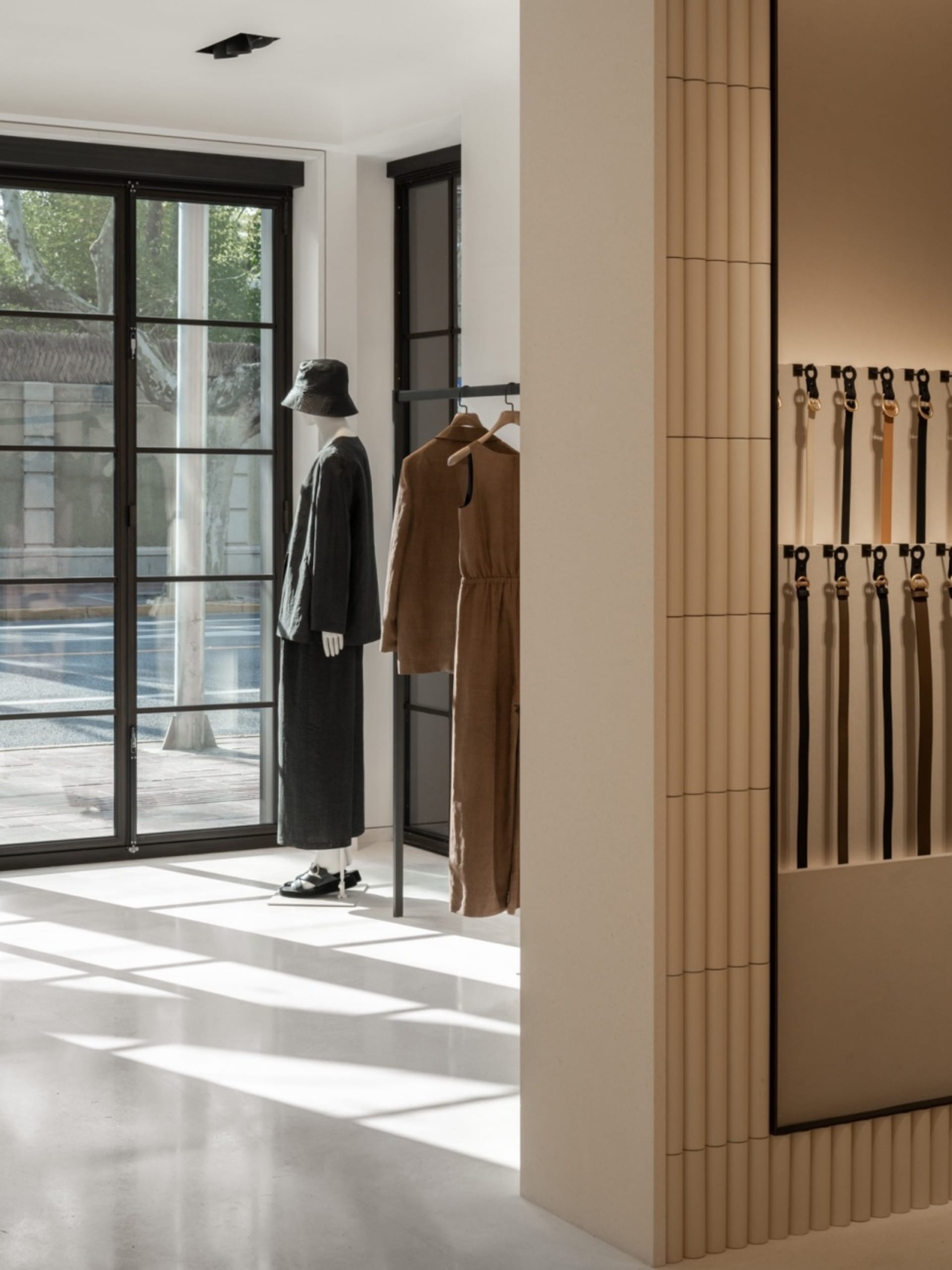 Urban retail storefront featuring minimalist clothing on mannequins and belts lined up on a wall.