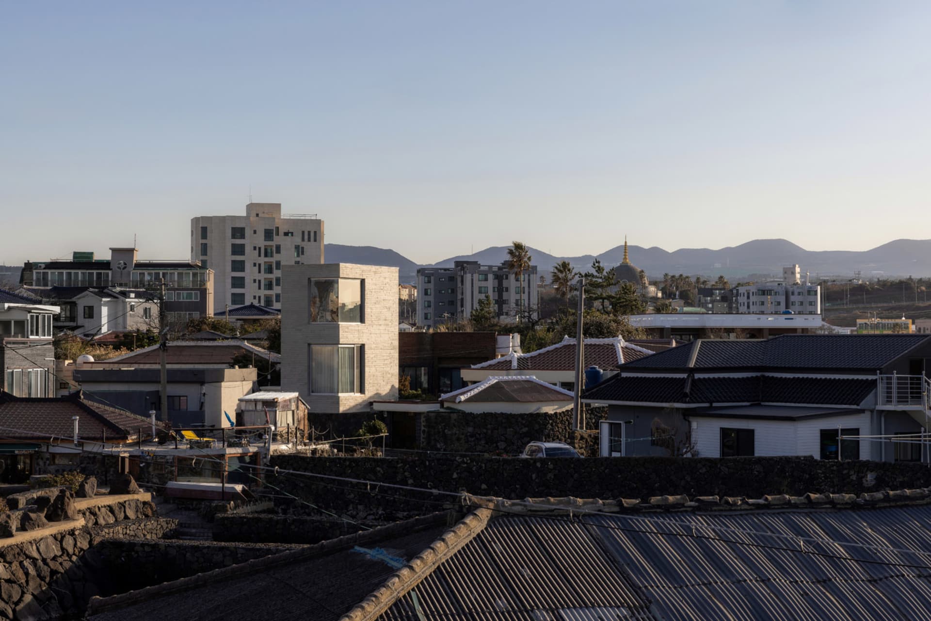 A cityscape view of rooftops with modern and traditional buildings, mountains in the background.