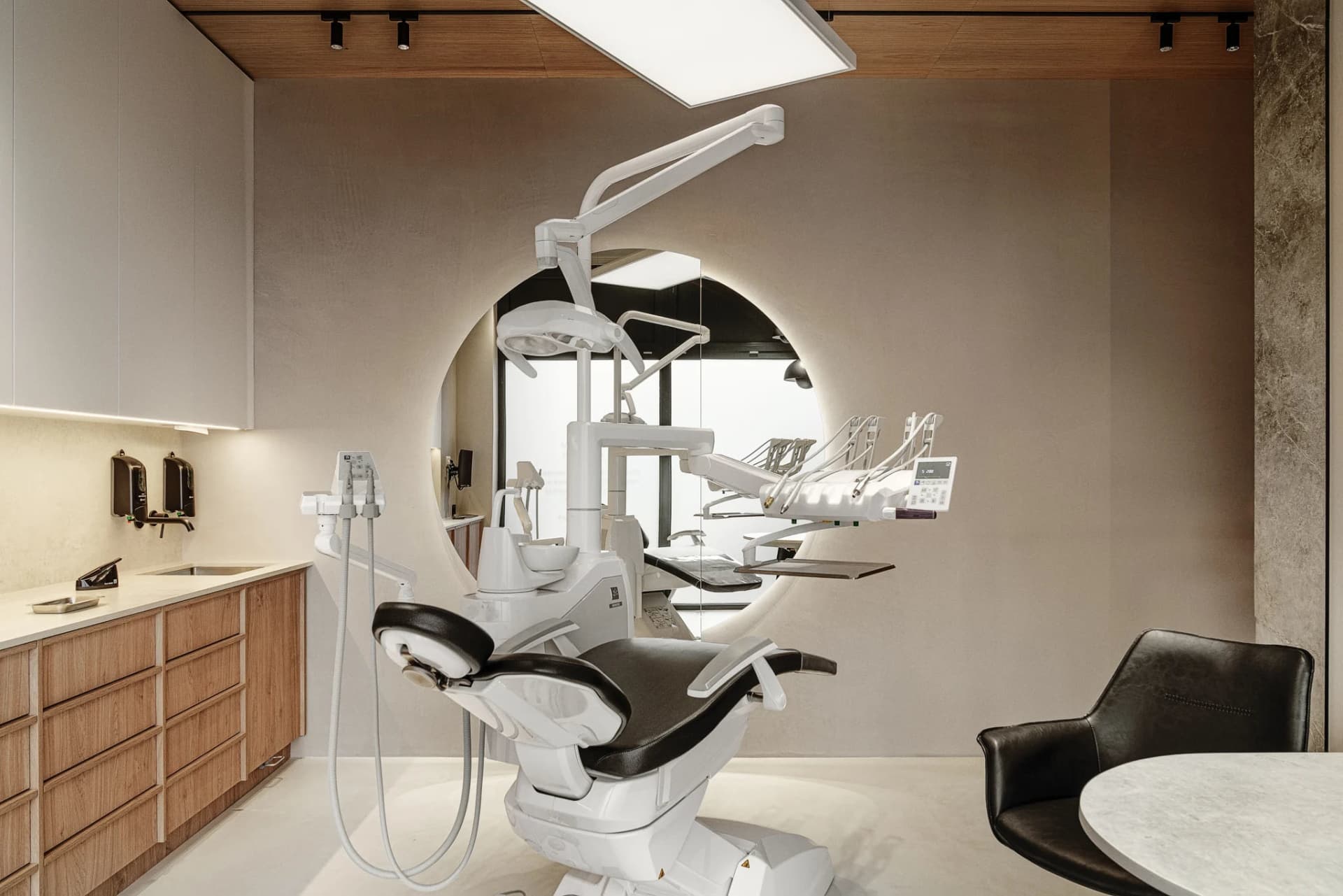 A minimalist dental office with a white dental chair and wooden cabinets.