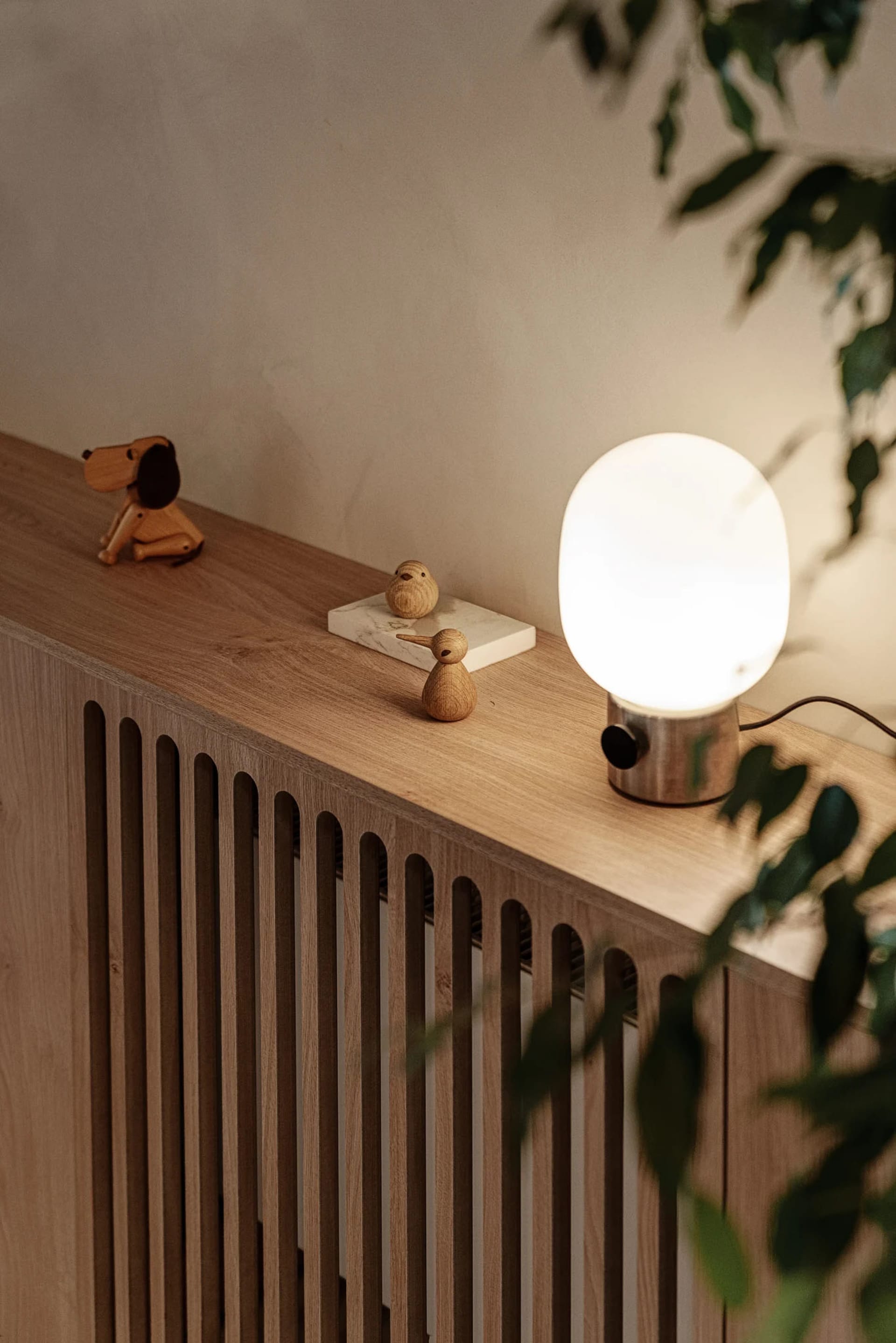 A modern living room featuring a wooden lamp and greenery on a wooden furniture piece.