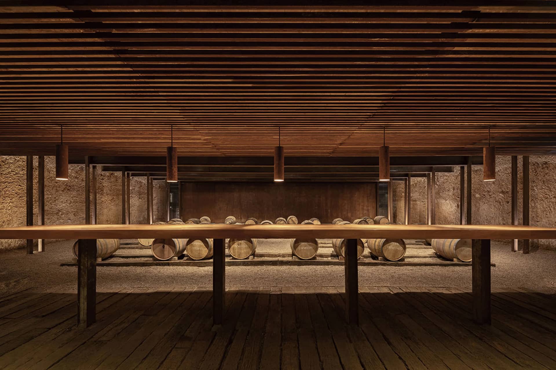 A spacious wine cellar with wooden barrels and a long wooden table.