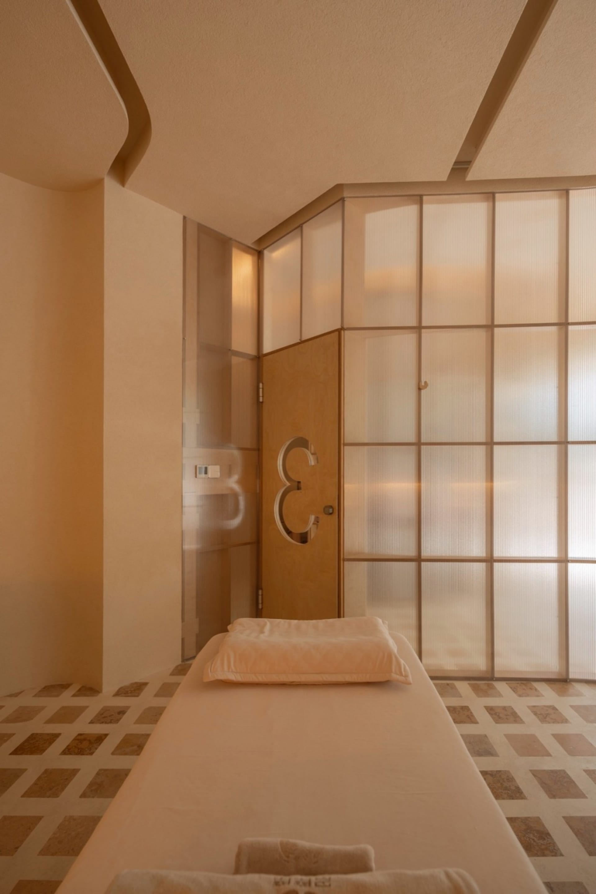 A minimalist treatment room with a bed, pillow, and sandstone materials.