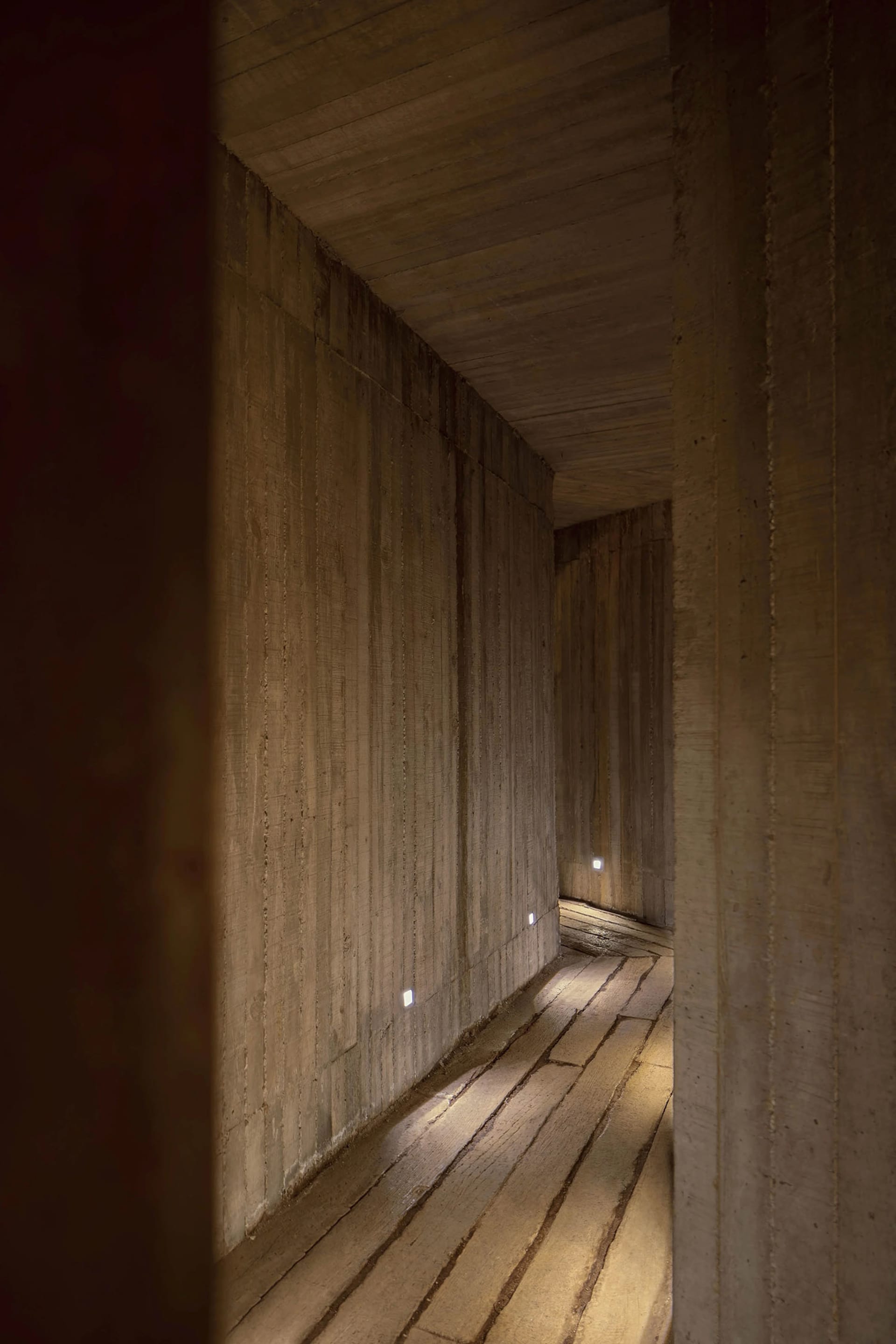 A modern corridor lined with concrete walls and illuminated by recessed lights.