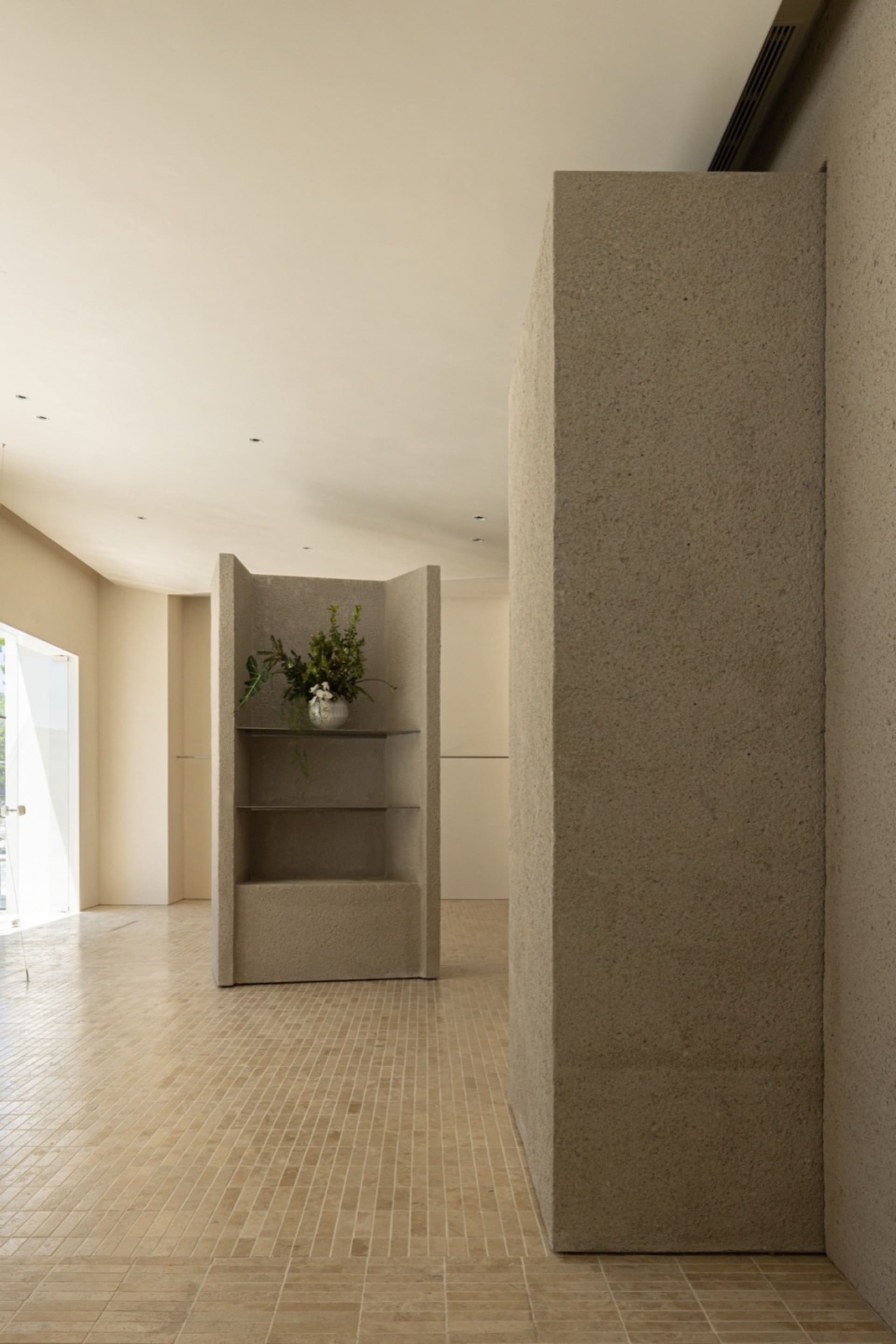 A minimalist room with concrete walls and floors, featuring a vase of flowers on a shelf.
