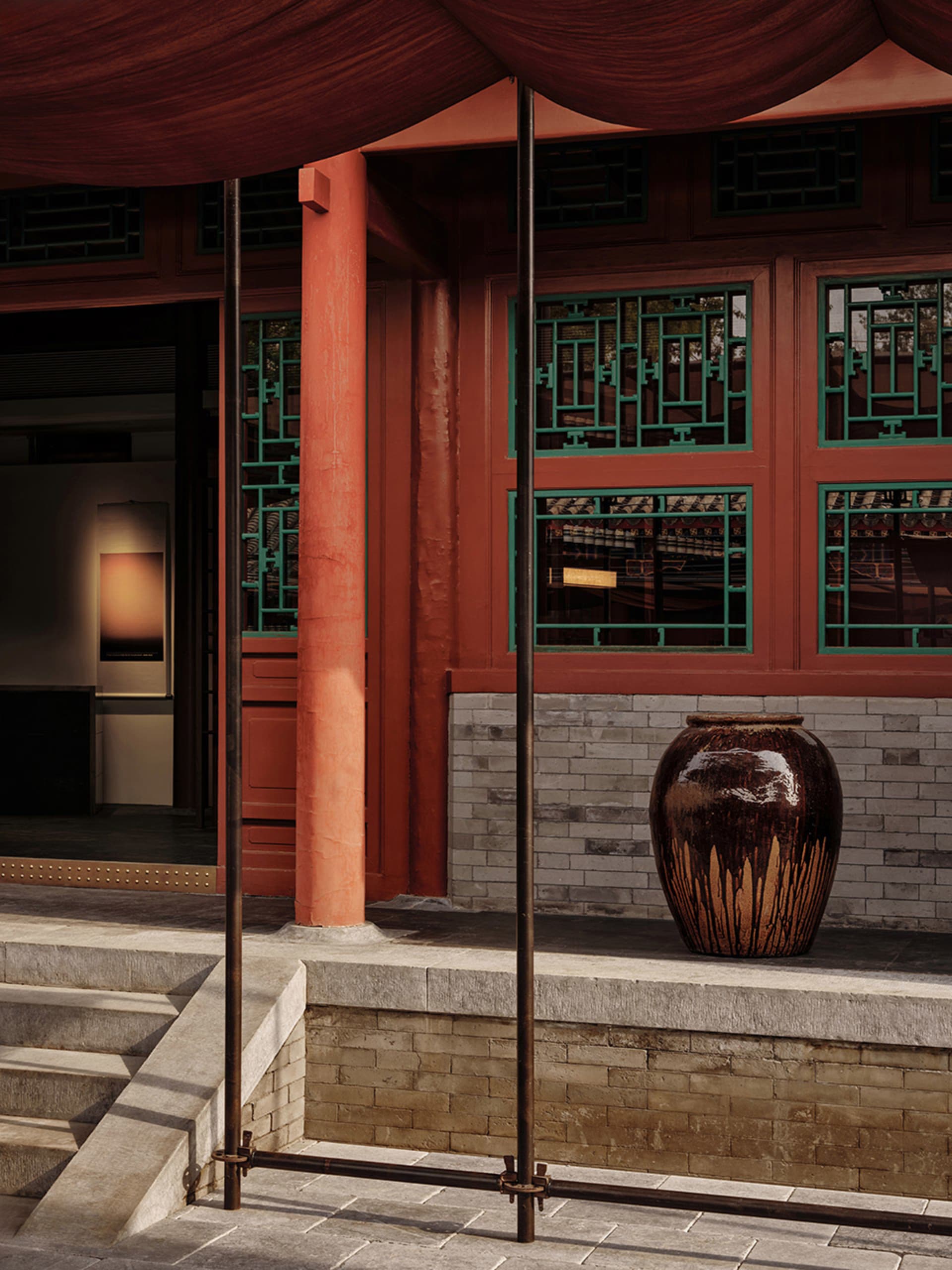 A traditional building exterior with a red wooden column, green-mesh windows, and a large brown vase.