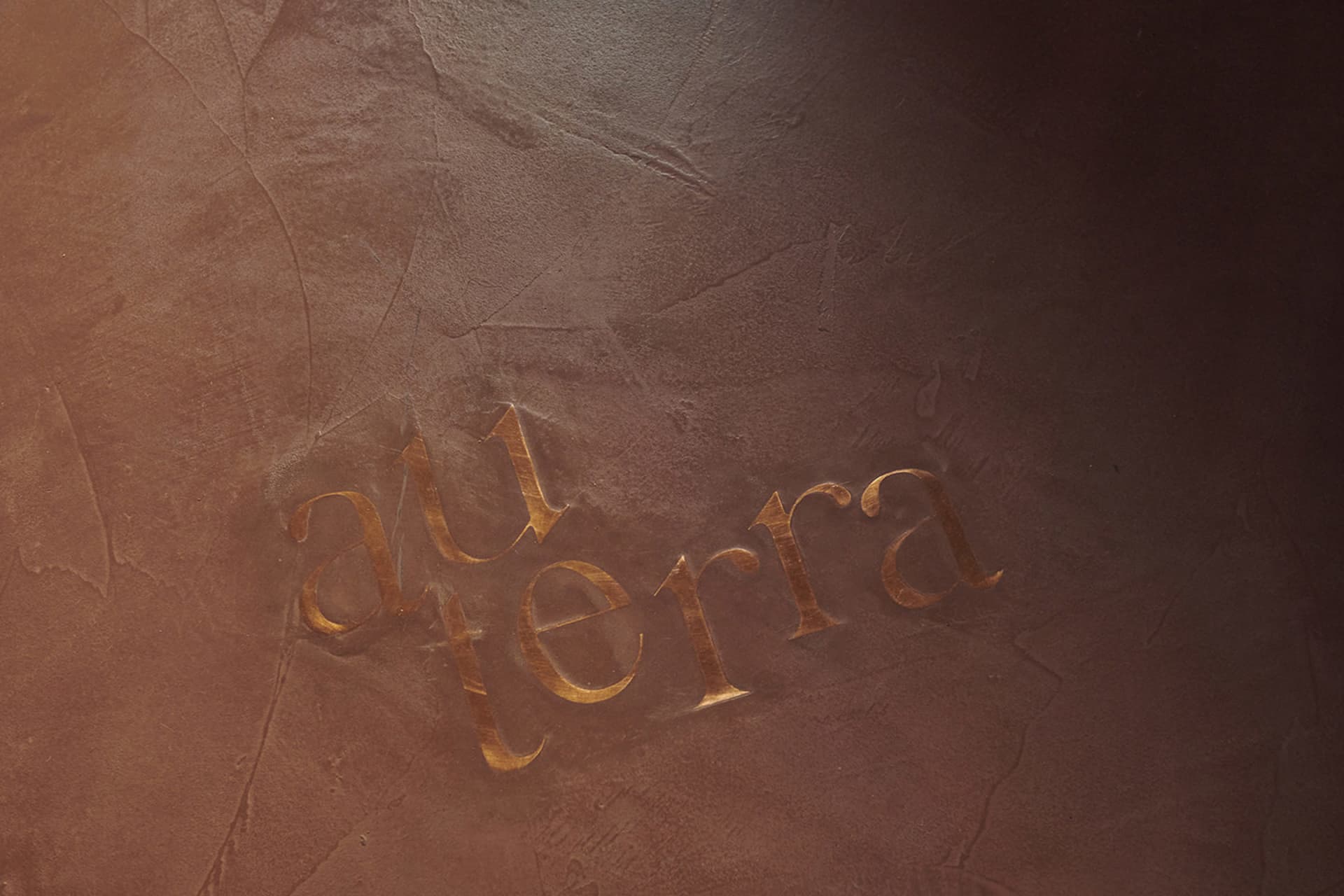 金色金屬雕刻銘文鑲嵌於質感牆面,呈現風格化字母拼寫「au terra」。