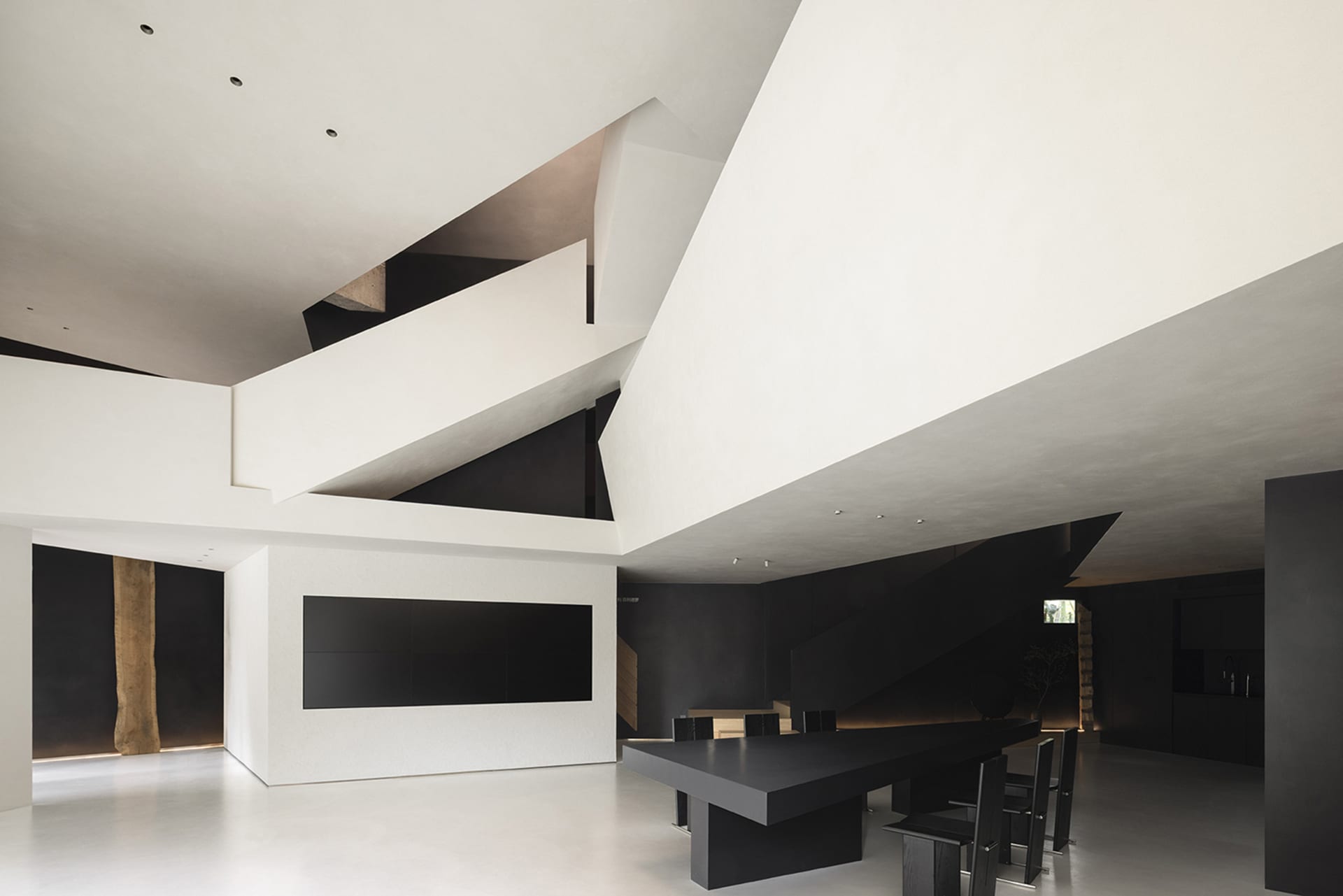 An image of a modern minimalist living room with concrete walls and floors, featuring sleek black furniture and a high, open