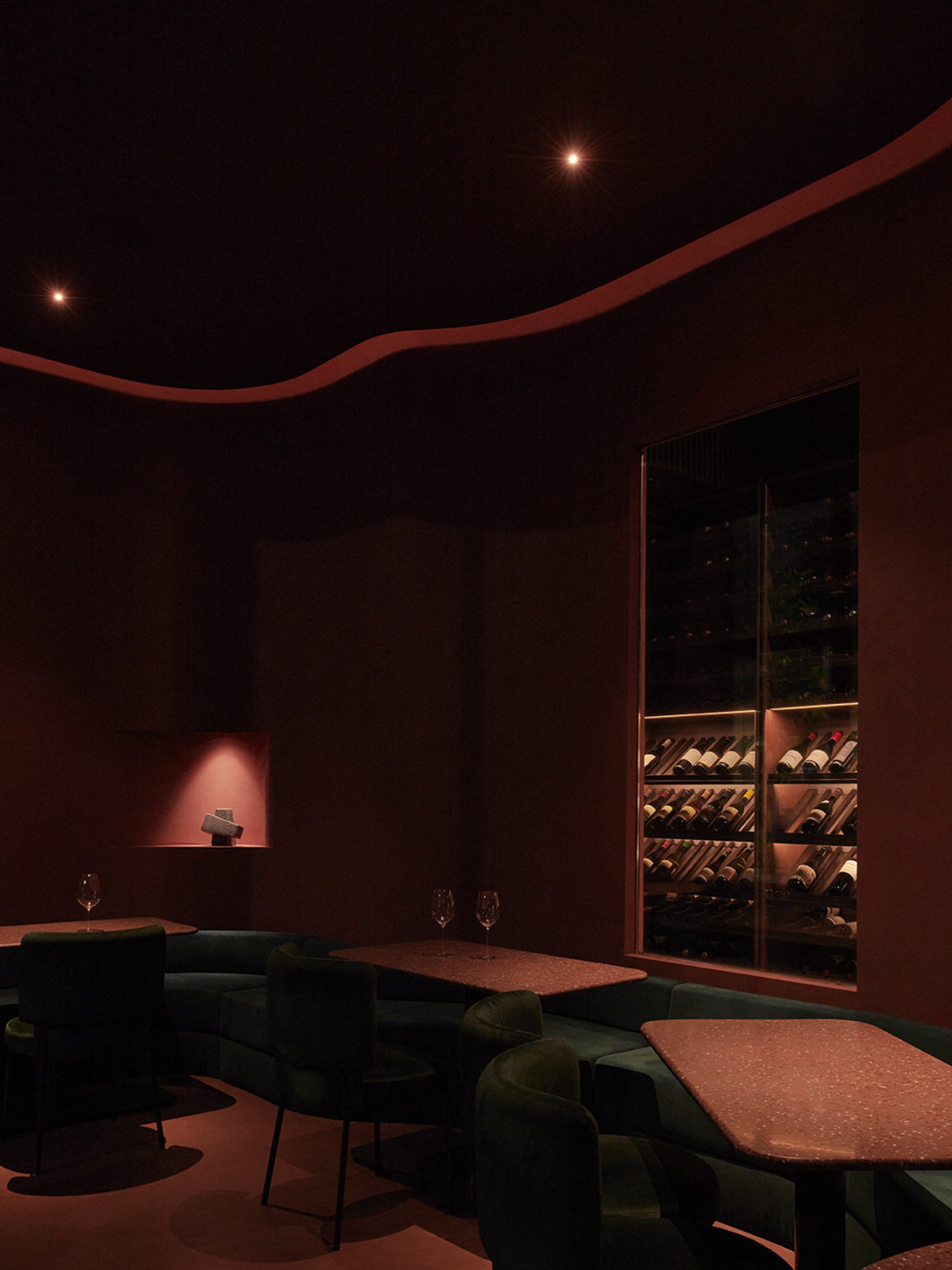 A dimly lit modern restaurant bar featuring a rustic, industrial ambiance with terrazzo tables and wine bottles on display.