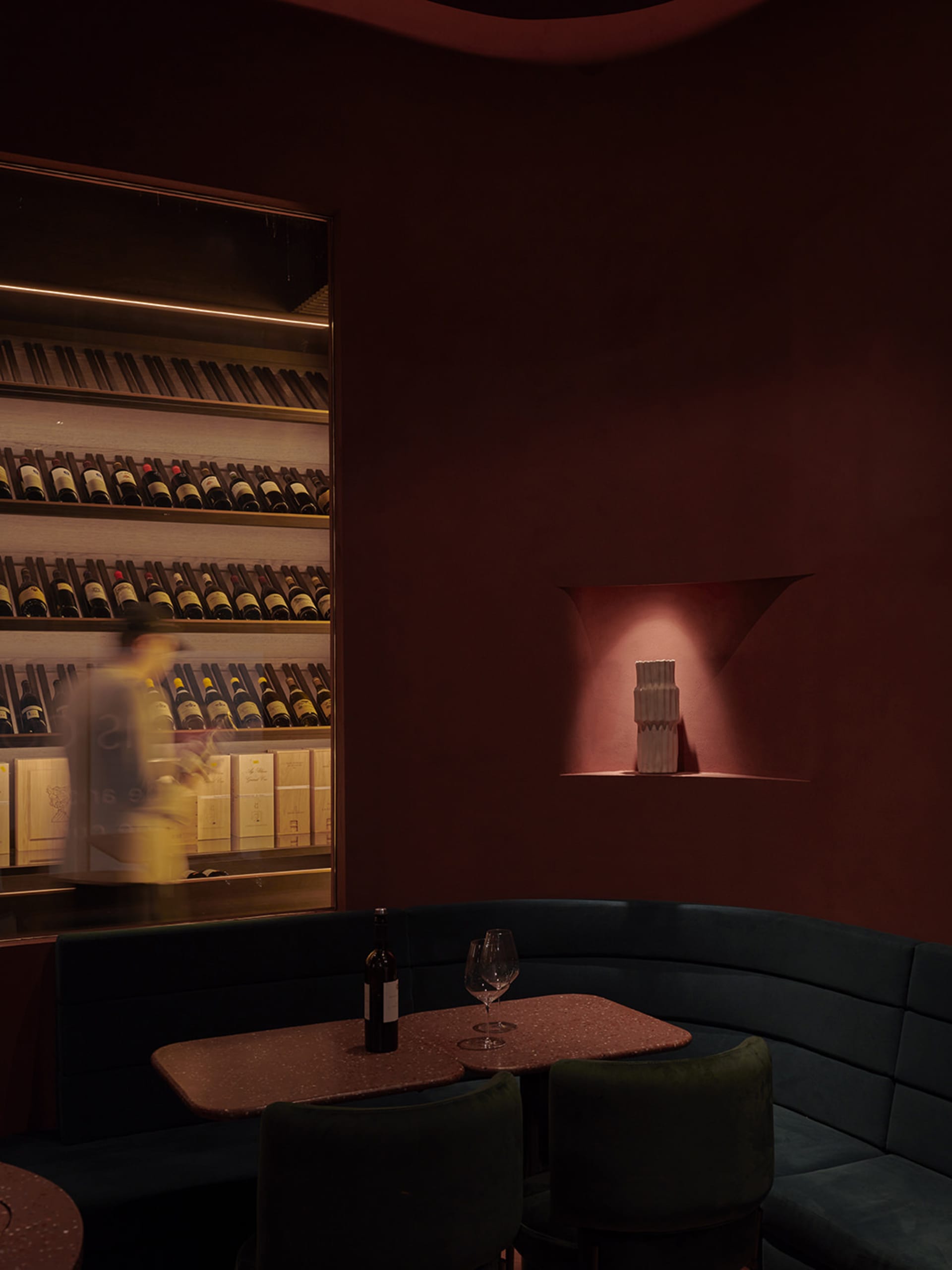 A cozy dining setup featuring a table with a bottle of wine and glasses, surrounded by upholstered seating and a terrazzo cou