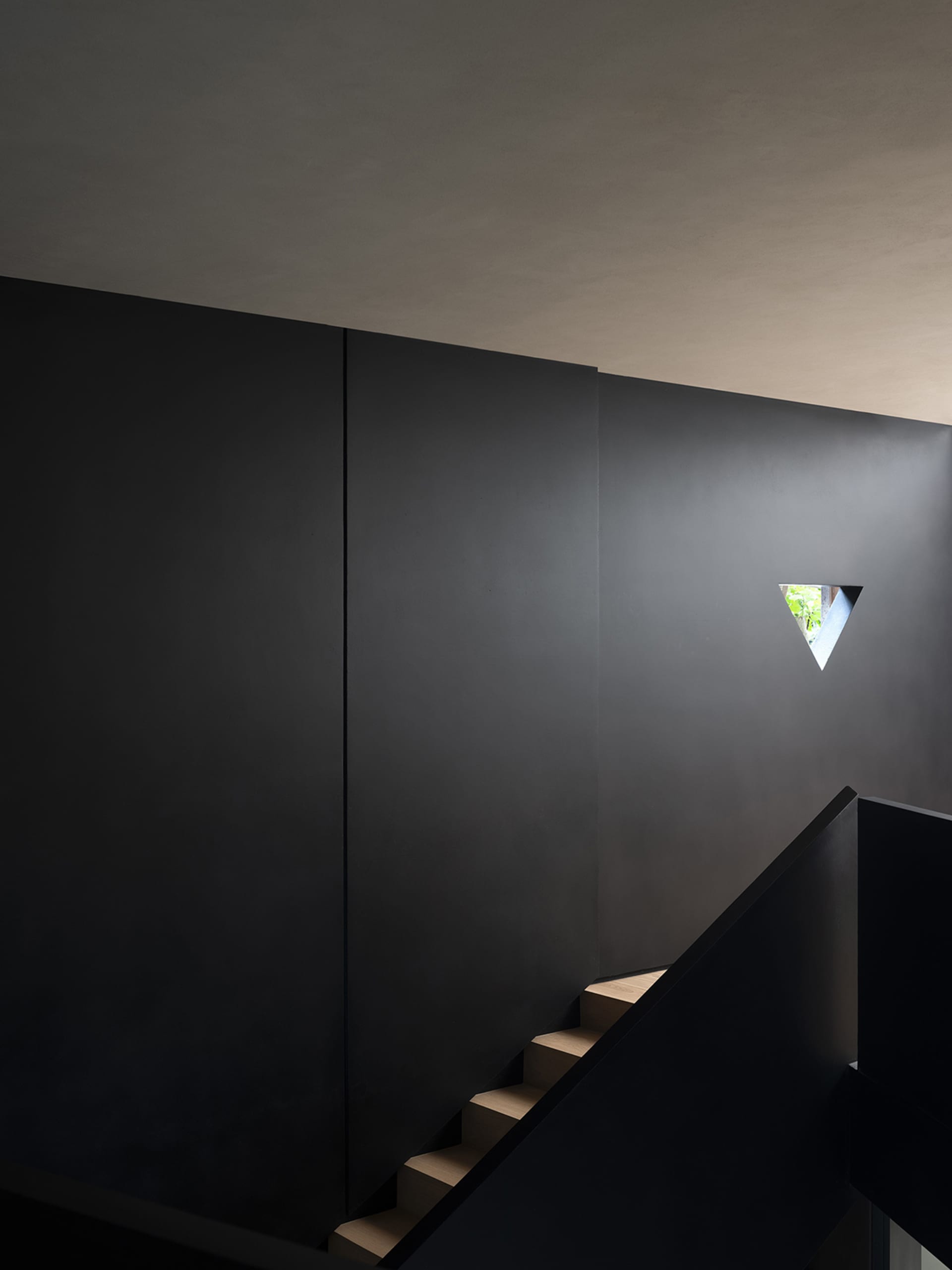 Modern, minimalist interior space with a black staircase, concrete walls, and a triangular window.