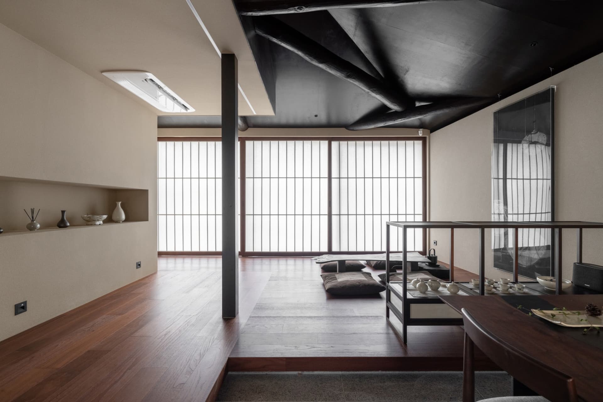 A modern indoor space featuring wooden flooring, minimalist furniture, and natural light through multiple windows.