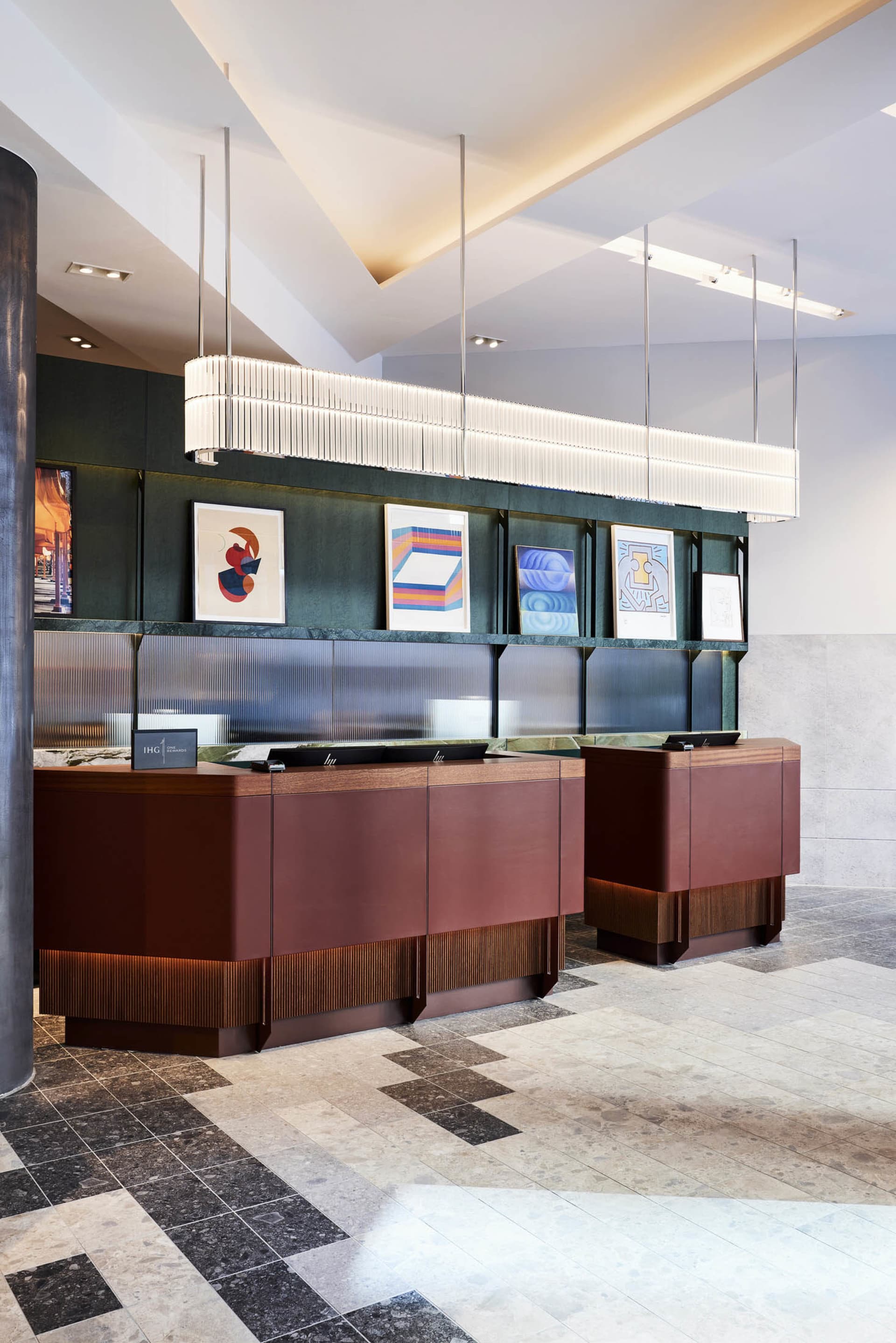 A modern reception desk made of marble and wood, featuring a hanging light fixture and framed artwork.