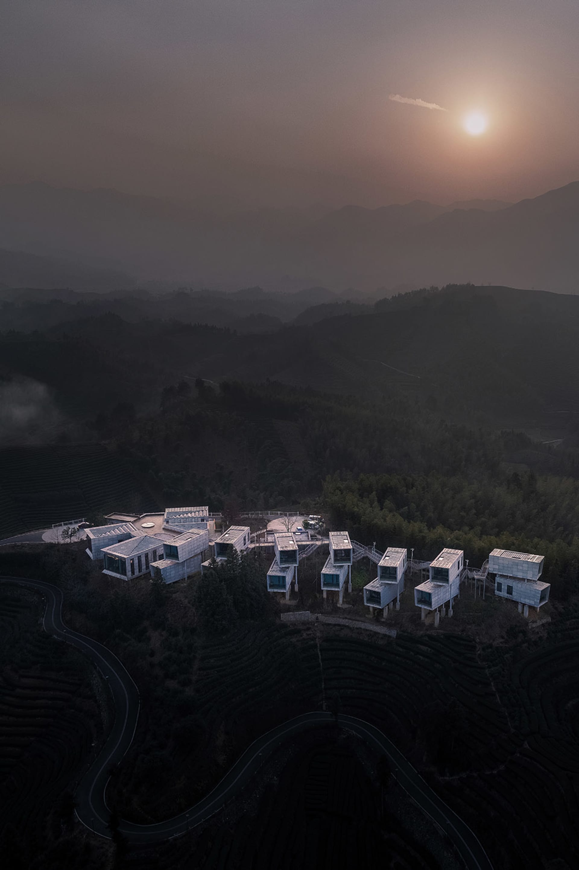 俯瞰山頂現代住宅建築,搭配梯田景觀與遠方山巒。