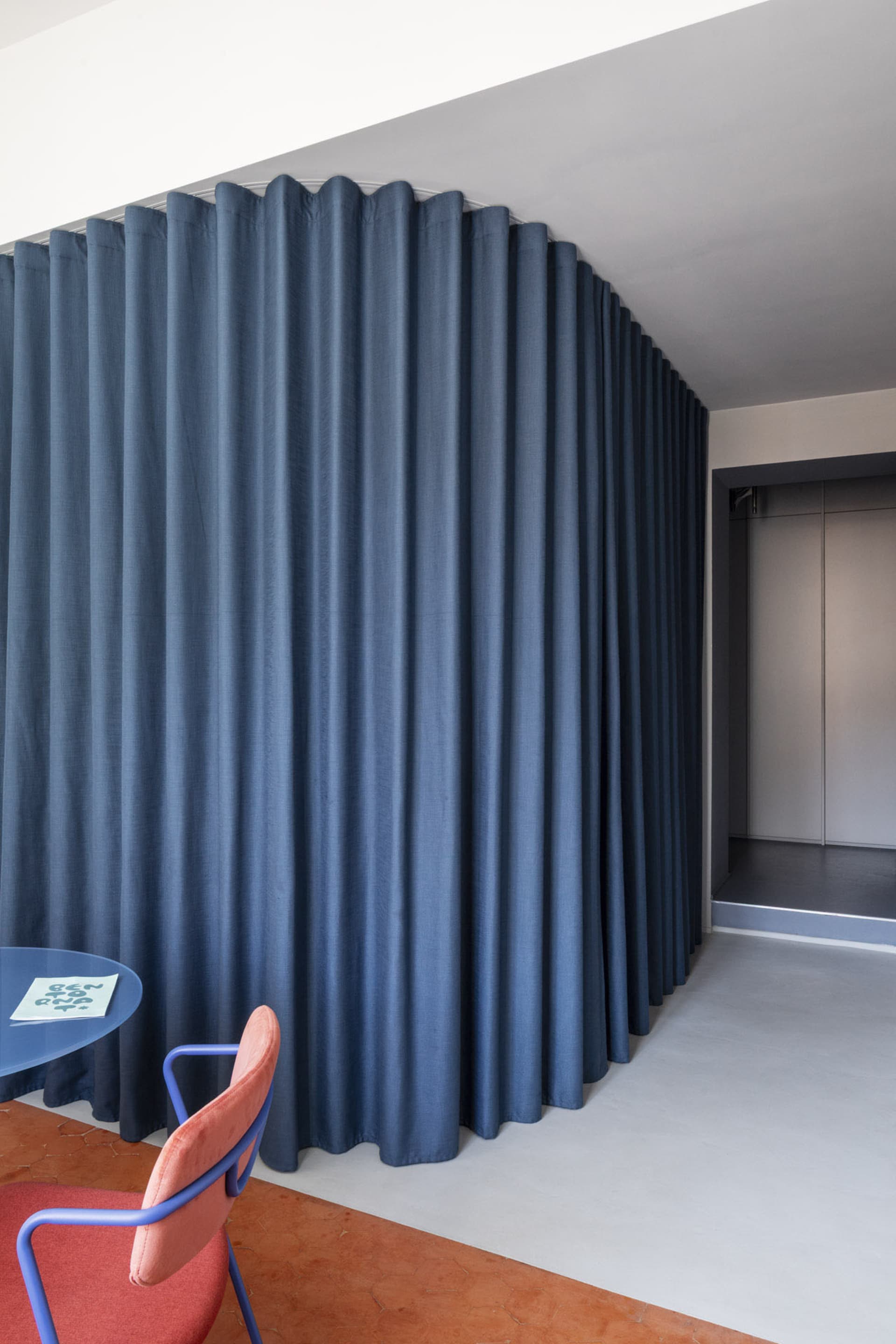A modern traditional space features blue curtains and a red chair.