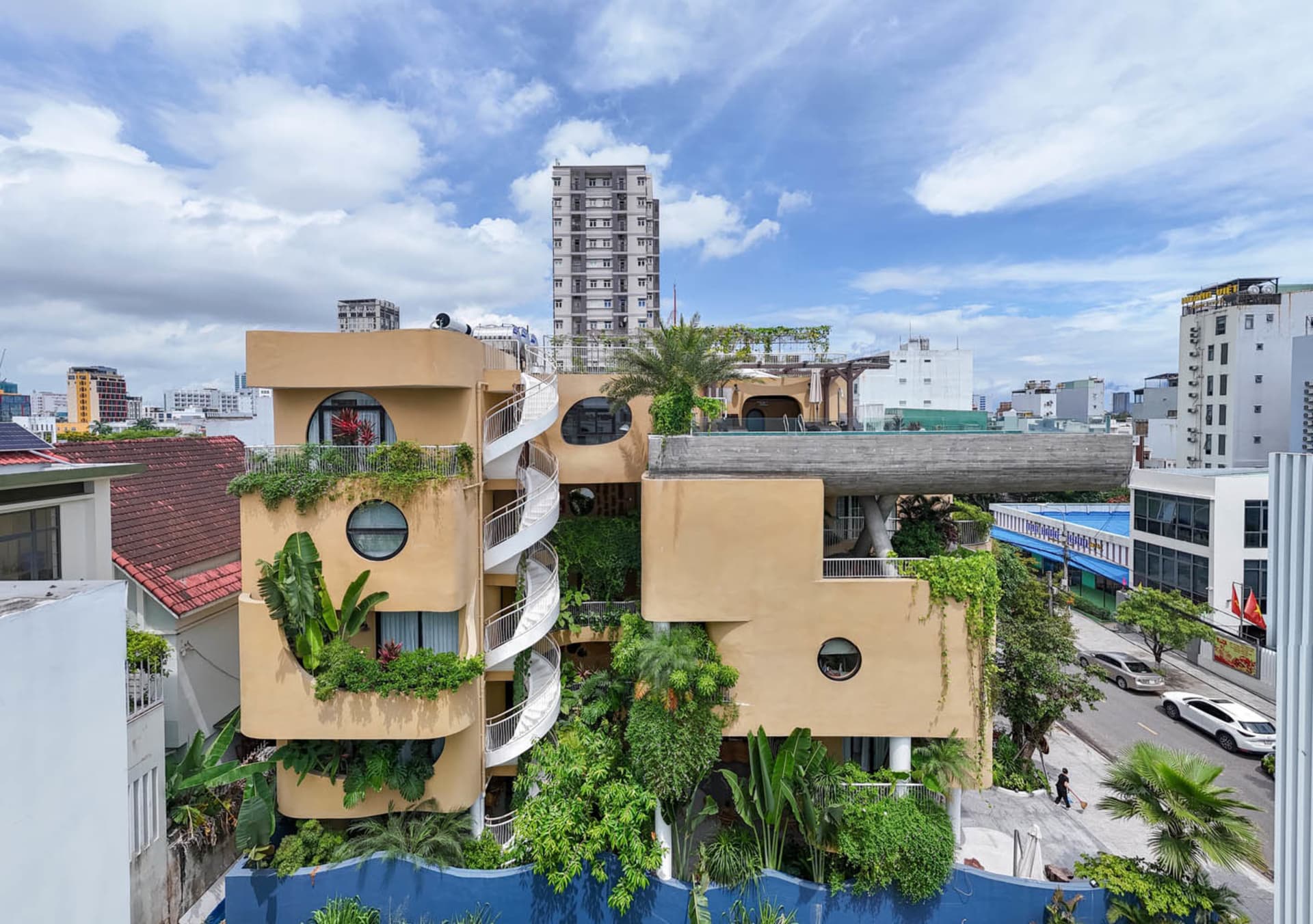 A modern building with concrete and glass exterior features greenery and balconies.