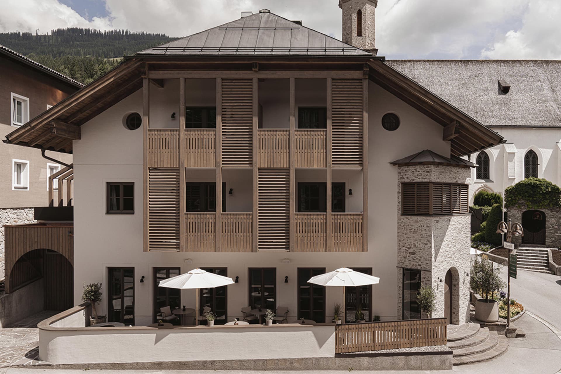 A modern hotel with stone and wooden exterior, featuring exterior balconies and a stone staircase.