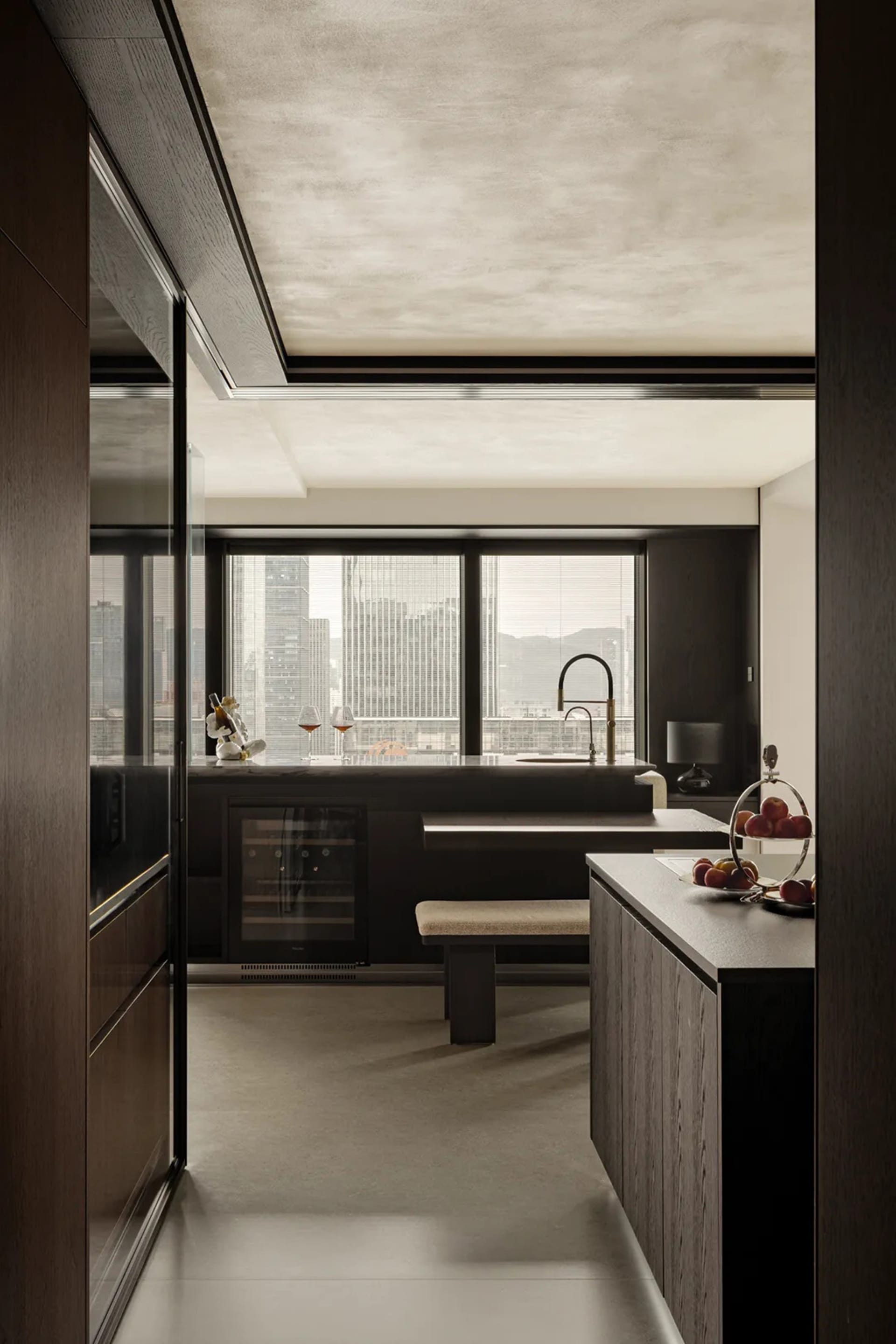 A modern kitchen with dark wooden elements and marble countertops, featuring a large window with a cityscape view.