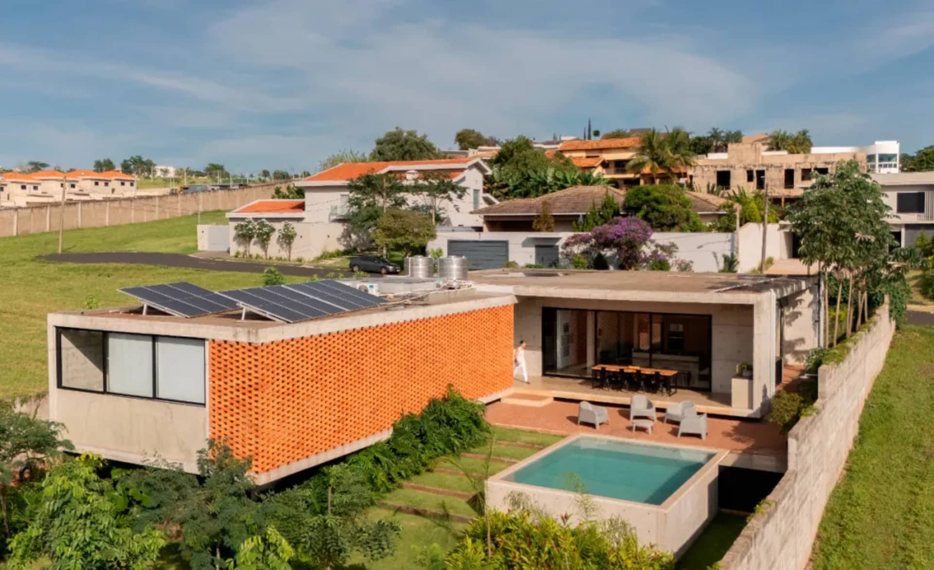 Modern residential house with concrete and orange brick architecture features a pool and greenery surrounding it.