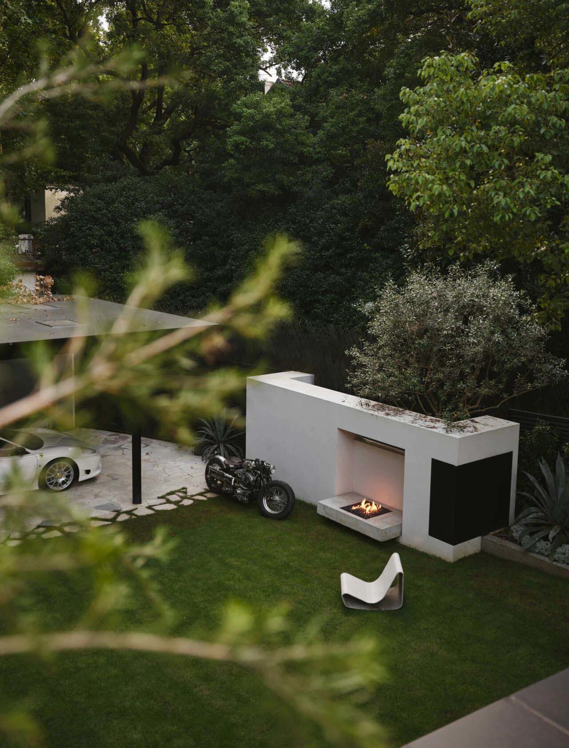 A modern outdoor living space with a concrete fireplace and greenery.