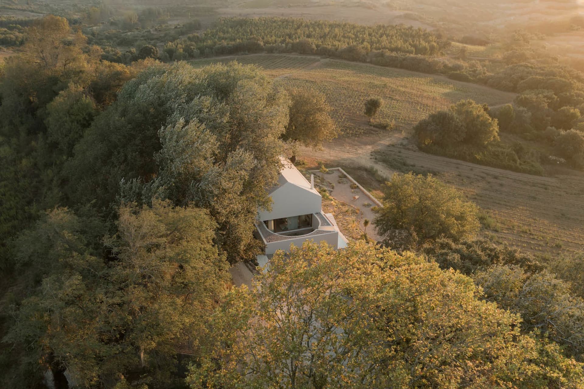 A minimalist house made of white concrete, surrounded by green trees and fields.