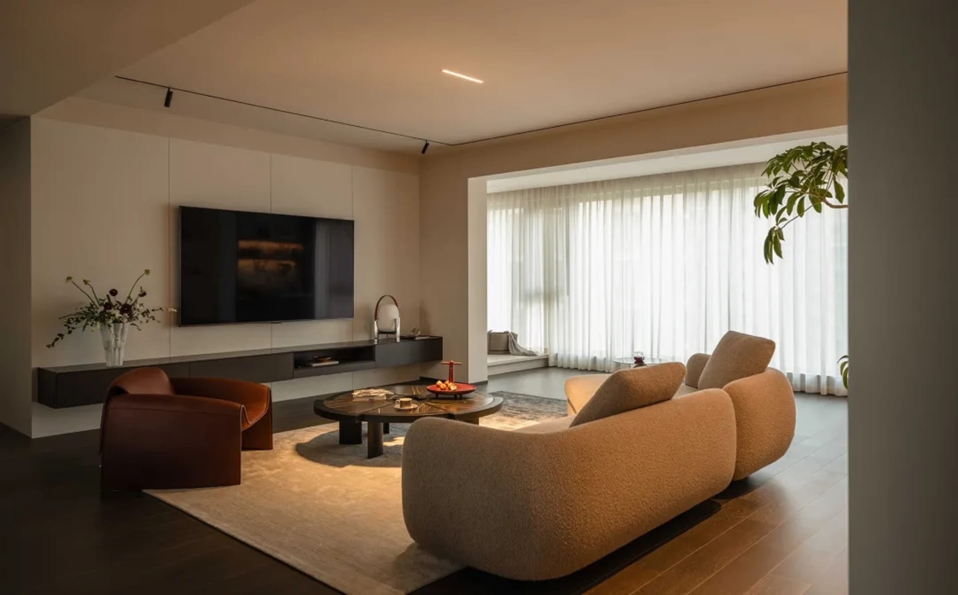 A minimalist living room featuring wooden flooring, fabric furniture, and glass elements.