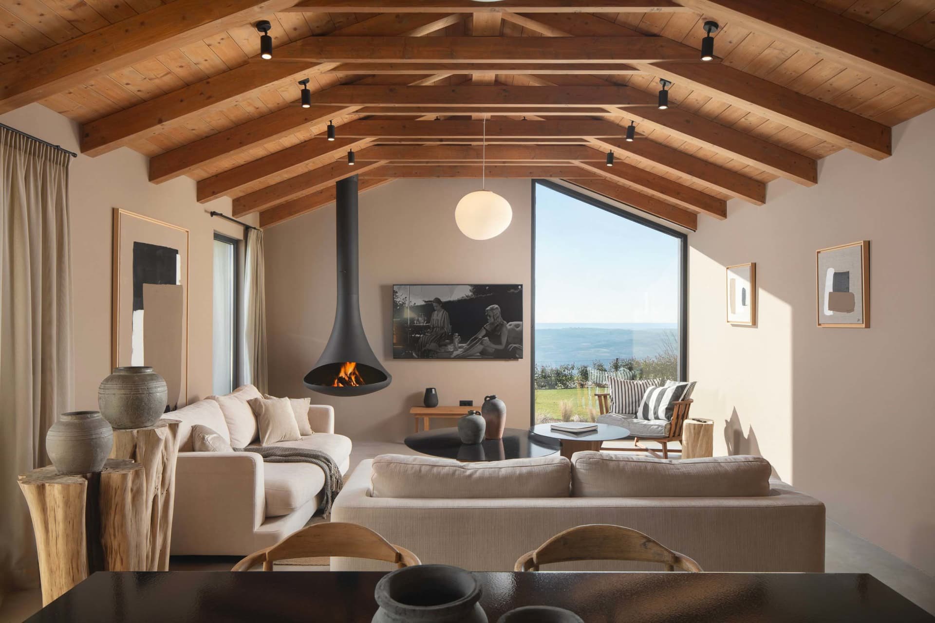 Modern living room with a wooden beam ceiling and a suspended fireplace.